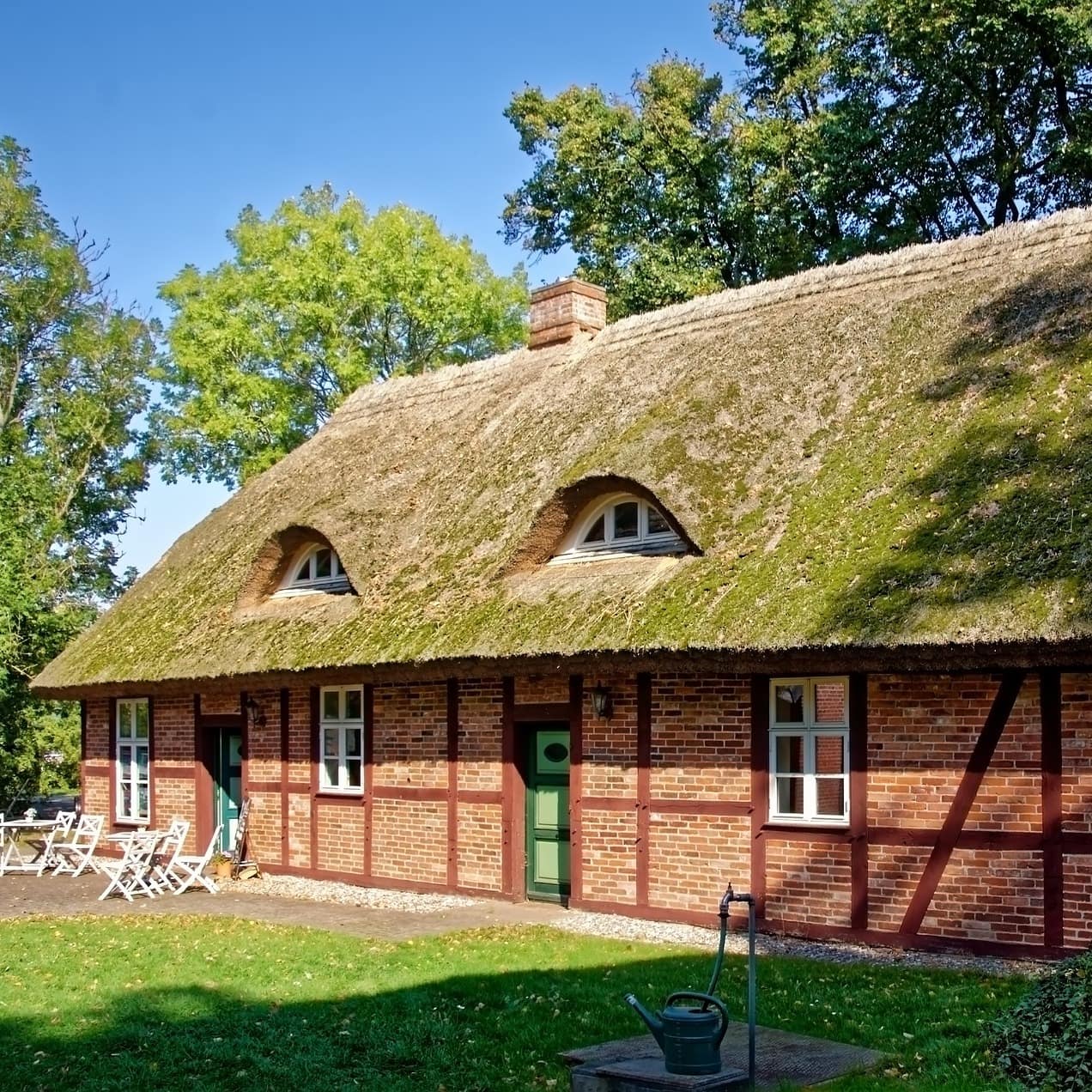 Blick auf ein typisches Haus mit Reetdach auf Rügen mit Garten, das Meer ist im Hintergrund zu erkennen
