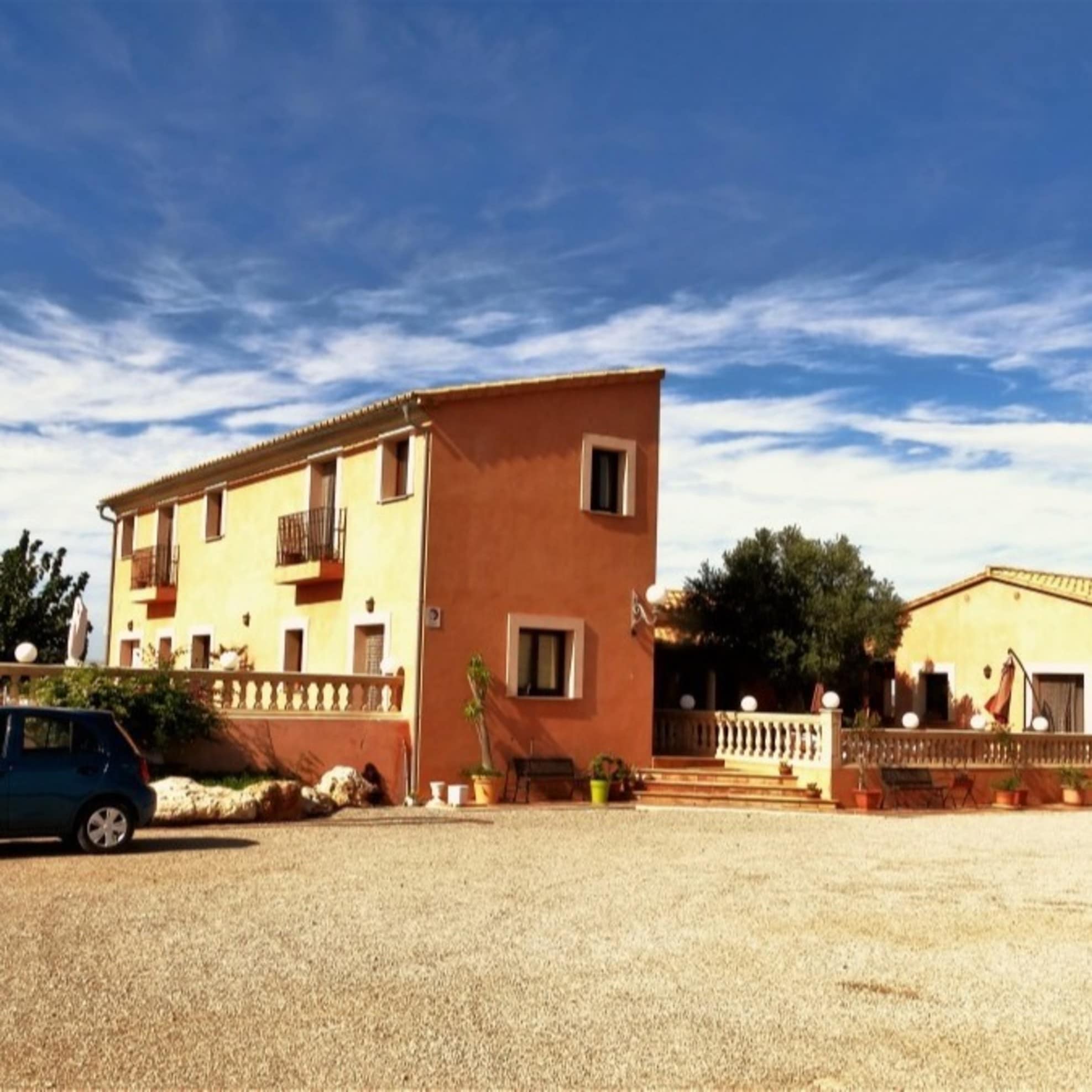 Finca vor blauem Himmel mit Parkplatz und Kleinwagen im Vordergrund