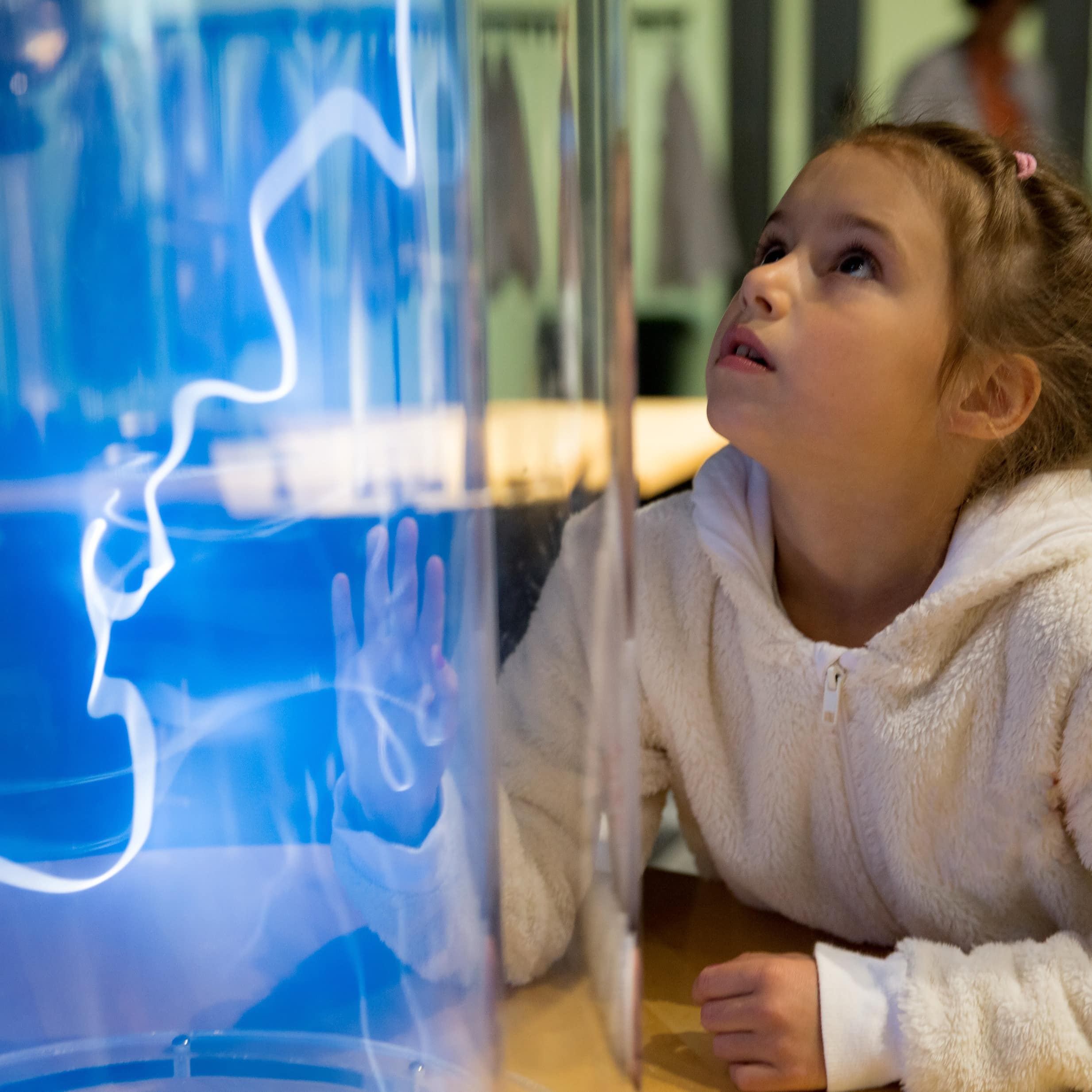 Ein Mädchen im Museum steht staunend vor einer runden Vitrine, in der sich Elektrizität entlädt.