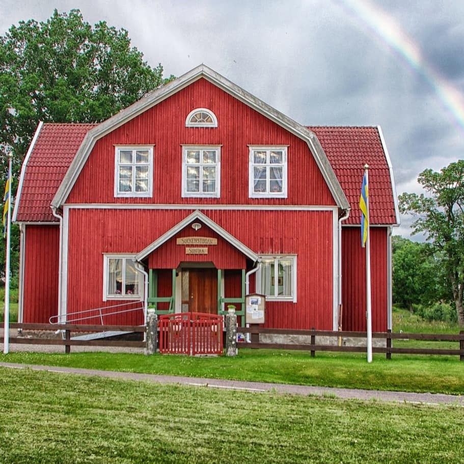 Ein typischen rotes zweistöckiges Holzhaus in Schweden mit Garten, im Hintergrund ist ein Regenbogen zu sehen.