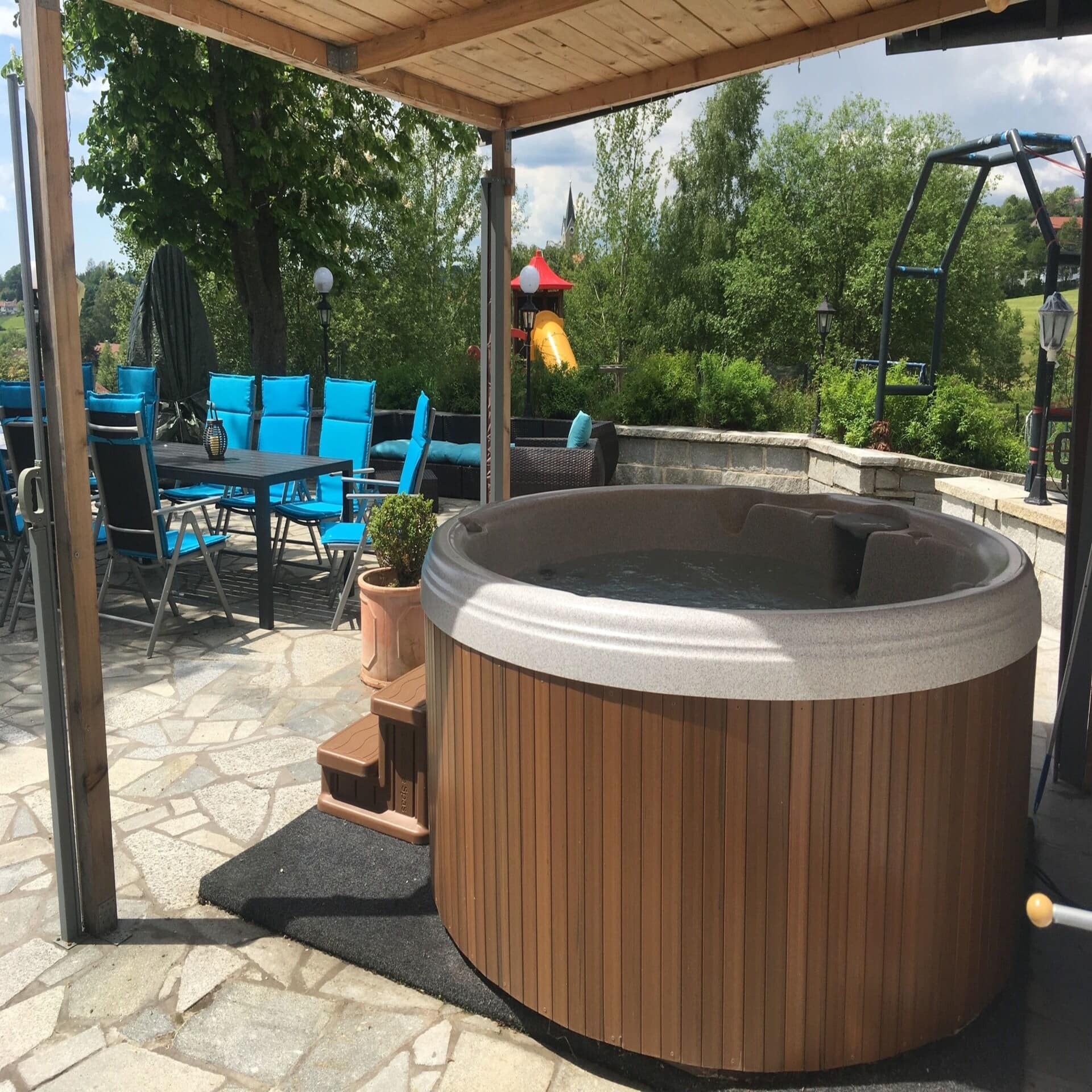 Terrasse mit Whirlpool und Tisch. Im Garten ist ein Klettergerüst zu sehen.