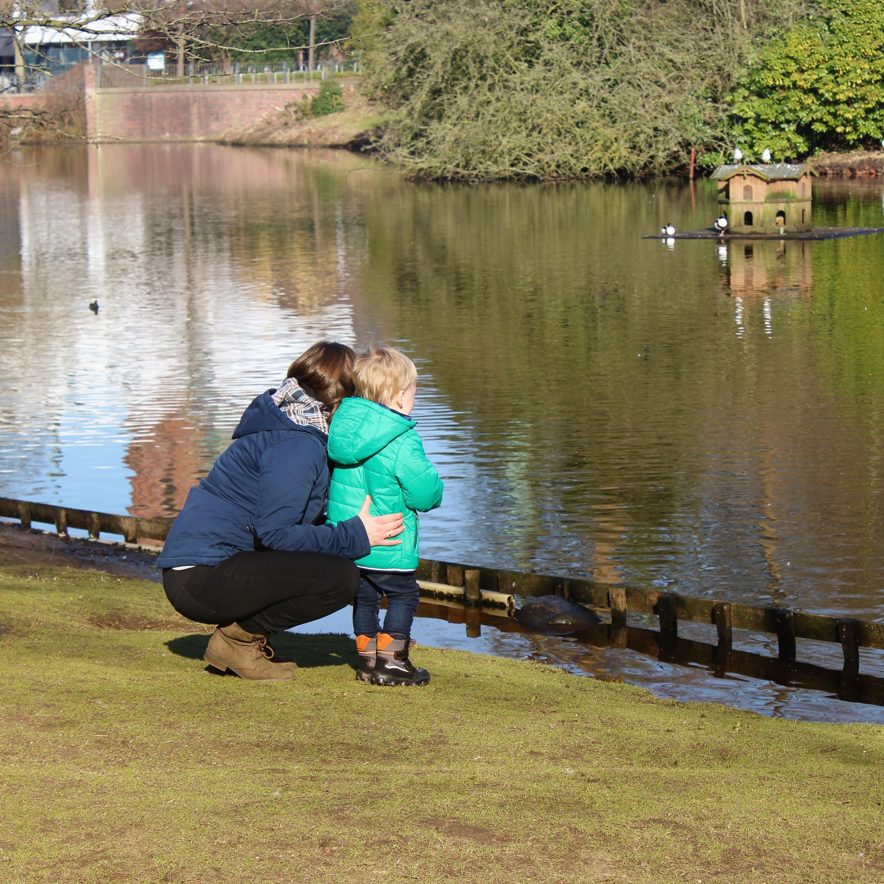 Mutter und kleiner Sohn beobachten Enten an einem Teich.