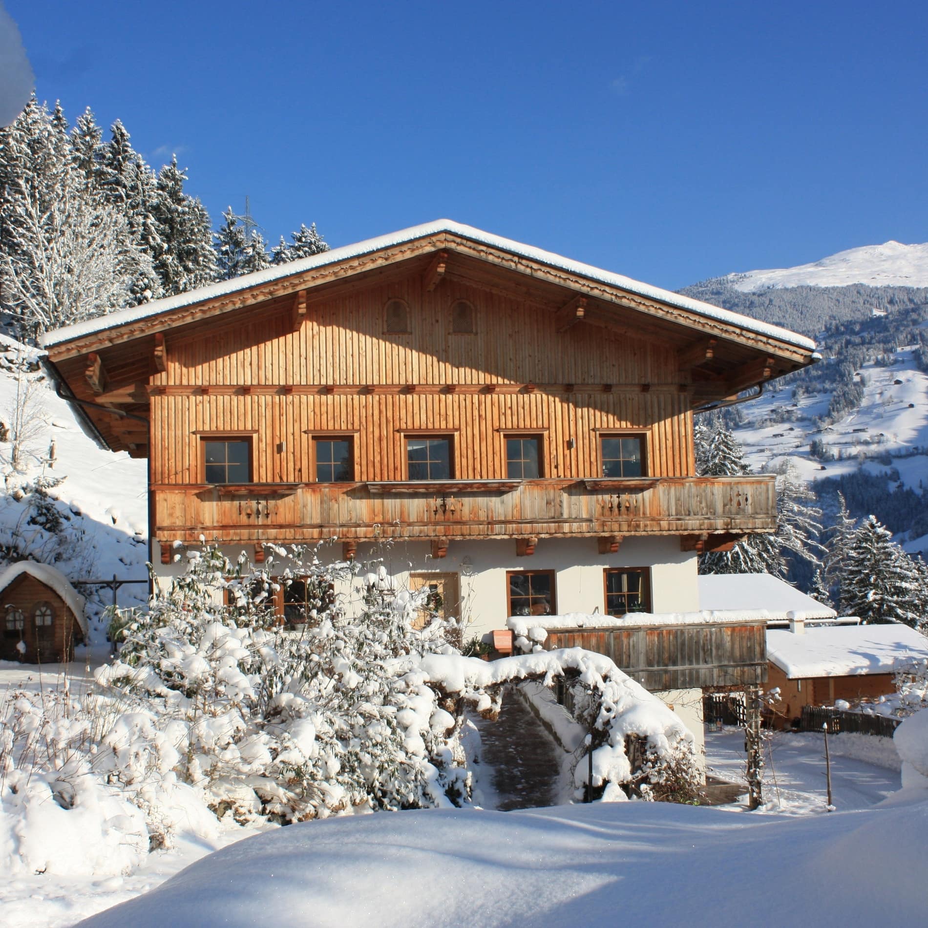 In einer Schneelandschaft steht ein Holzhaus mit durchgehendem Balkon an der Fassade 