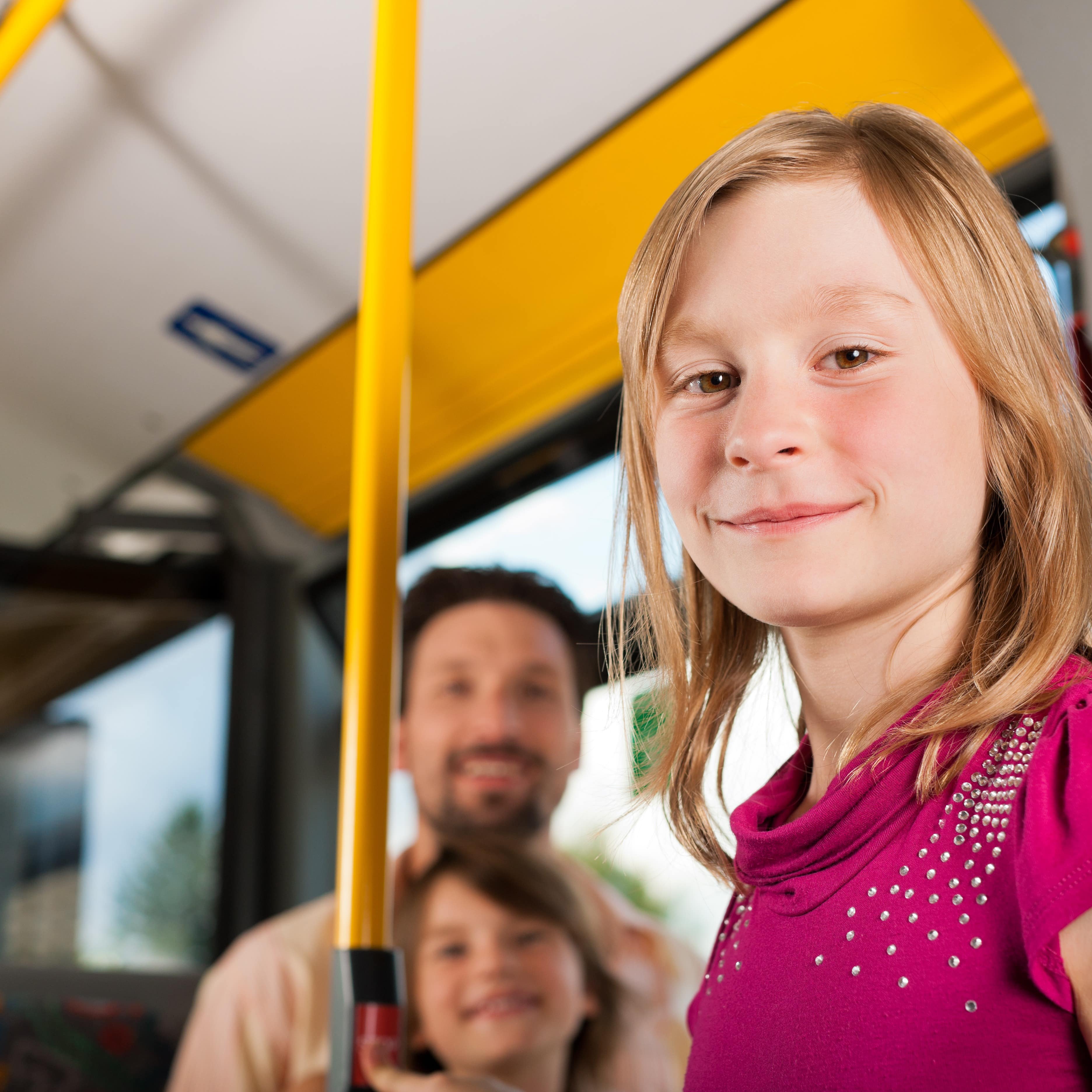 Mädchen in pinkem T-Shirt im Bus lächelt in die Kamera.