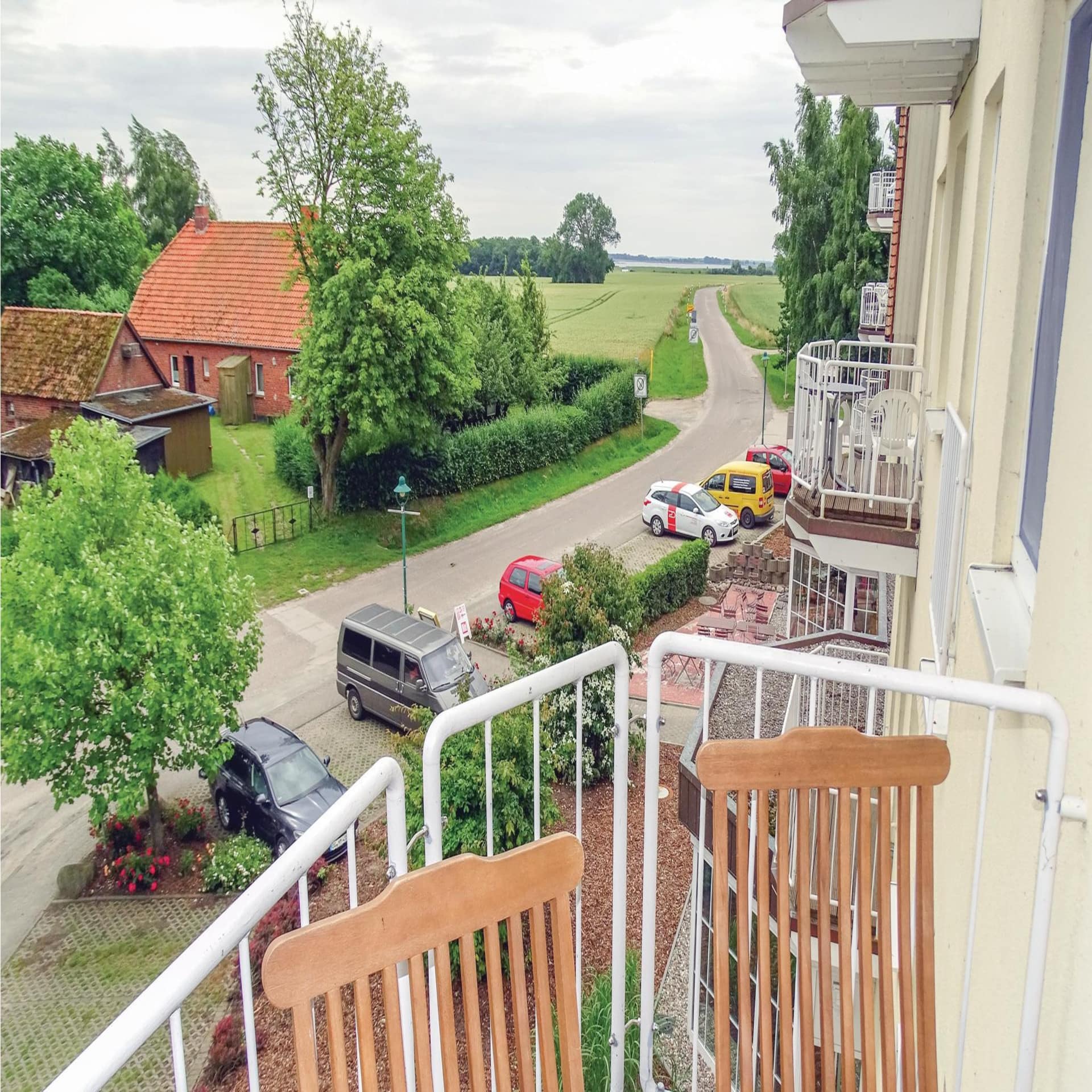 Blick vom Balkon eines Meerfamilienhauses auf eine Feldstraße, im Hintergrund schimmert das Meer.