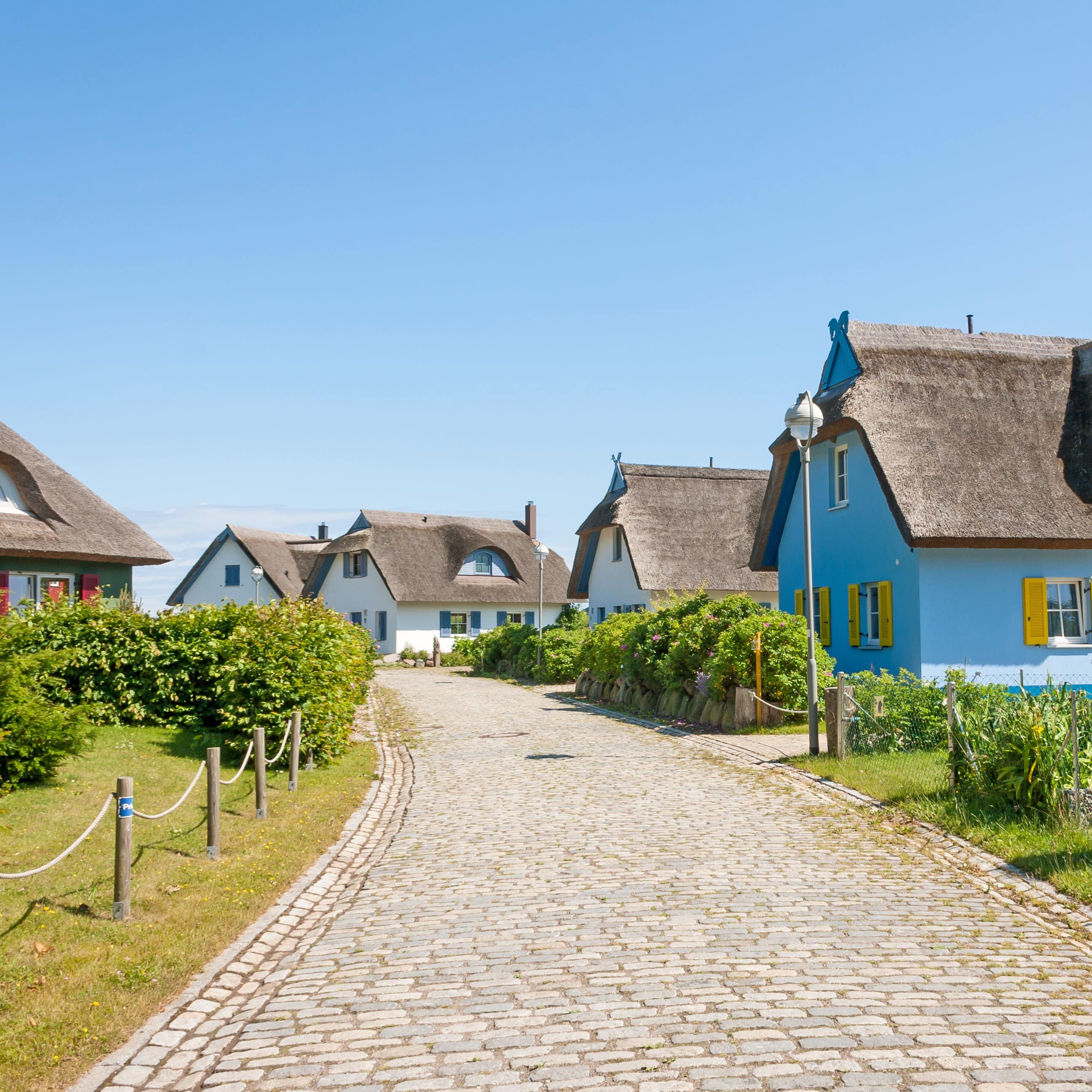 Ein Kopfsteinpflasterweg, links und rechts Reetdachhäuser.