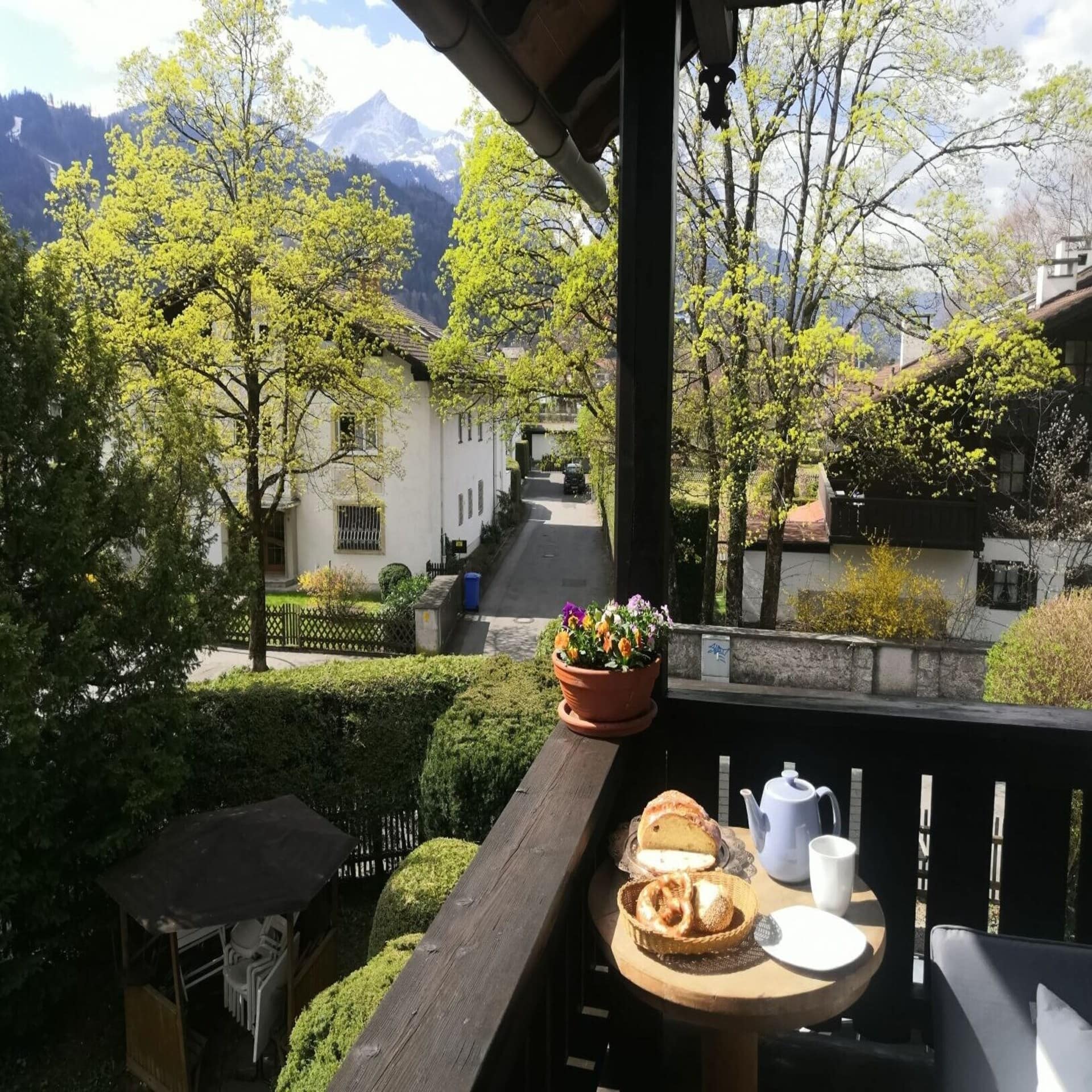 Balkon mit kleinem Frühstückstisch und Blick auf die Umgebung und die Berge. Es ist Frühling, die Sonne scheint.