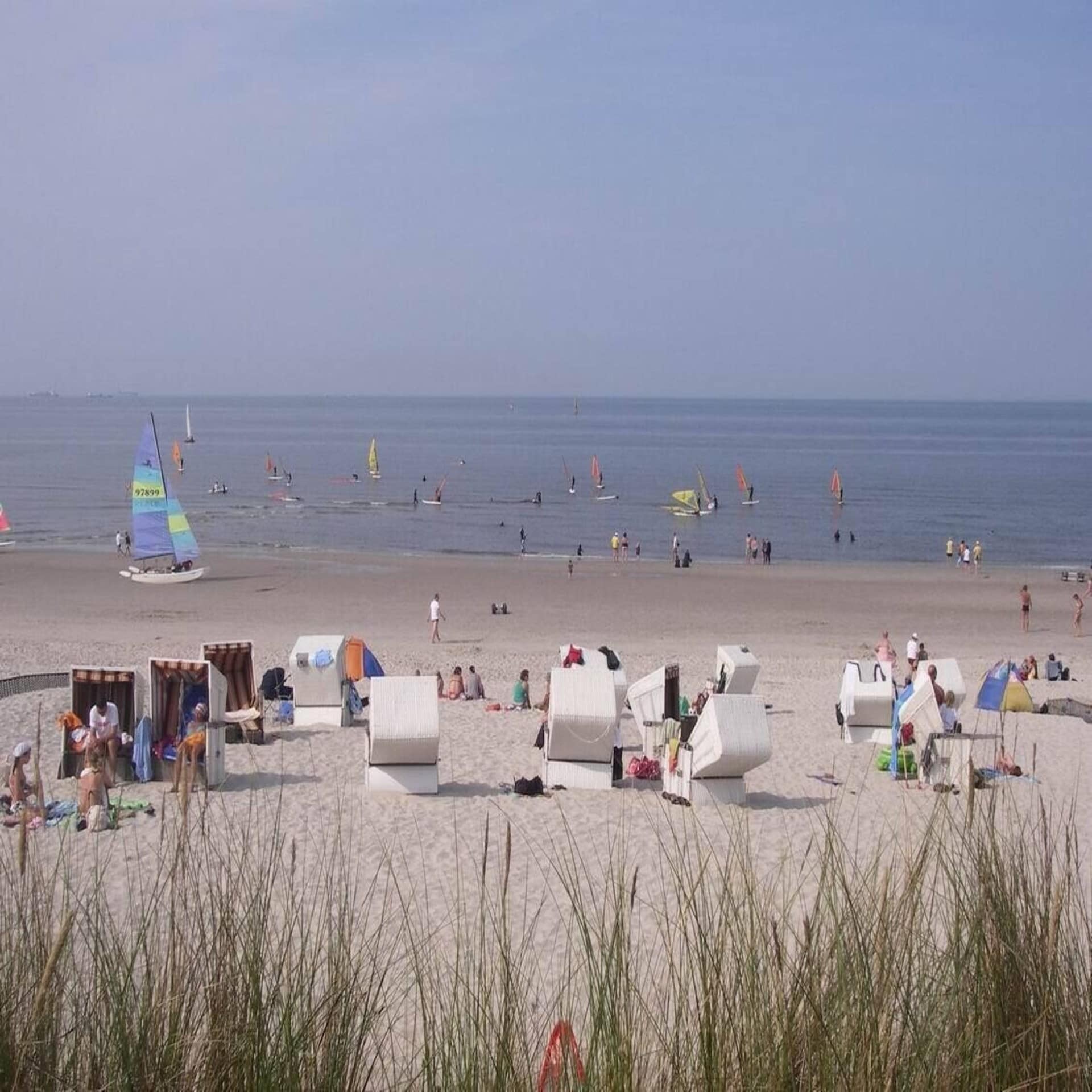 Strandleben von Wangerooge. Leute in Strandkörben und im Wasser. Einige Surfer sind im Wasser.