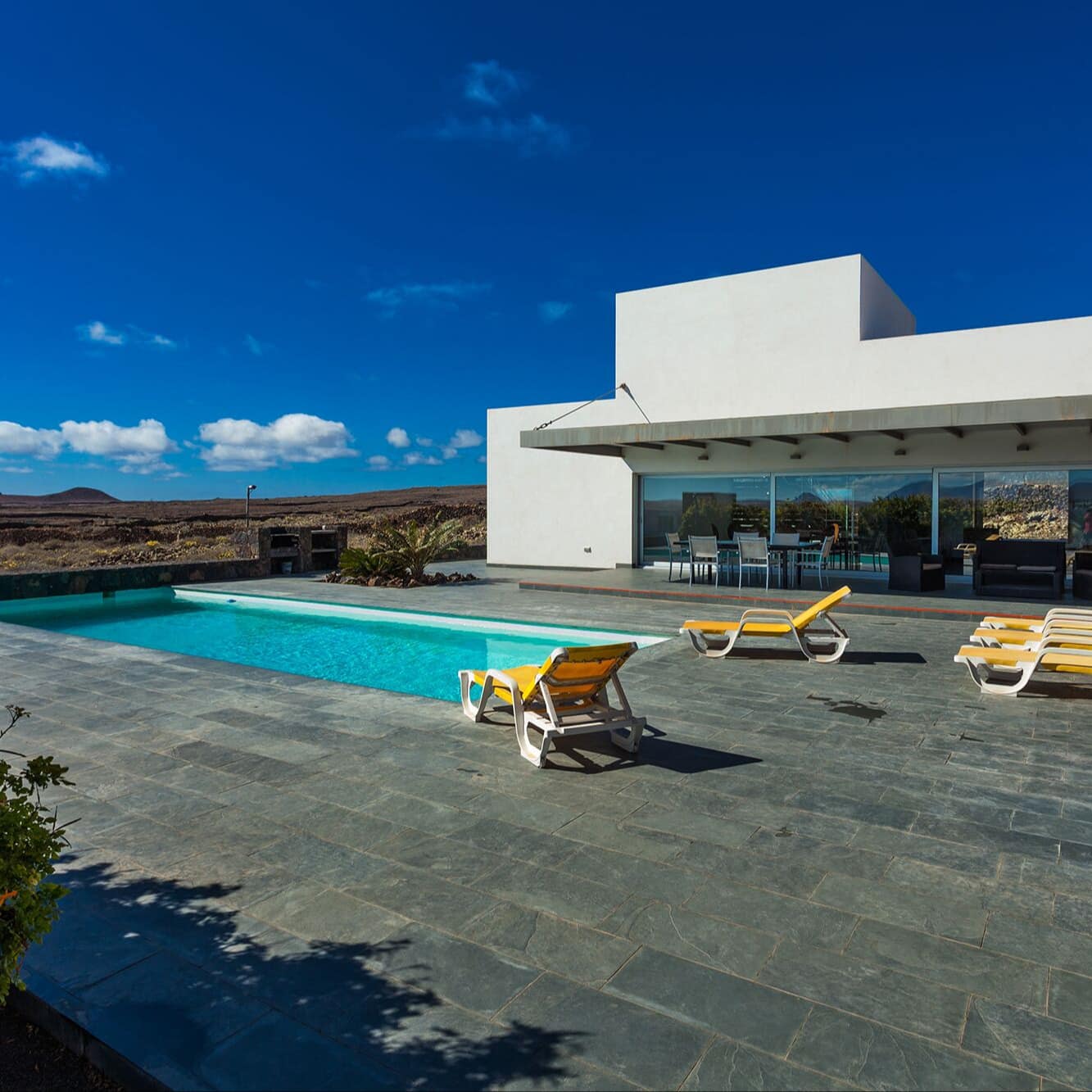 Modernes Ferienhaus mit Pool auf Fuerteventura, umgeben von einer großen Terrasse mit Liegen und Blick auf die Vulkanlandschaft
