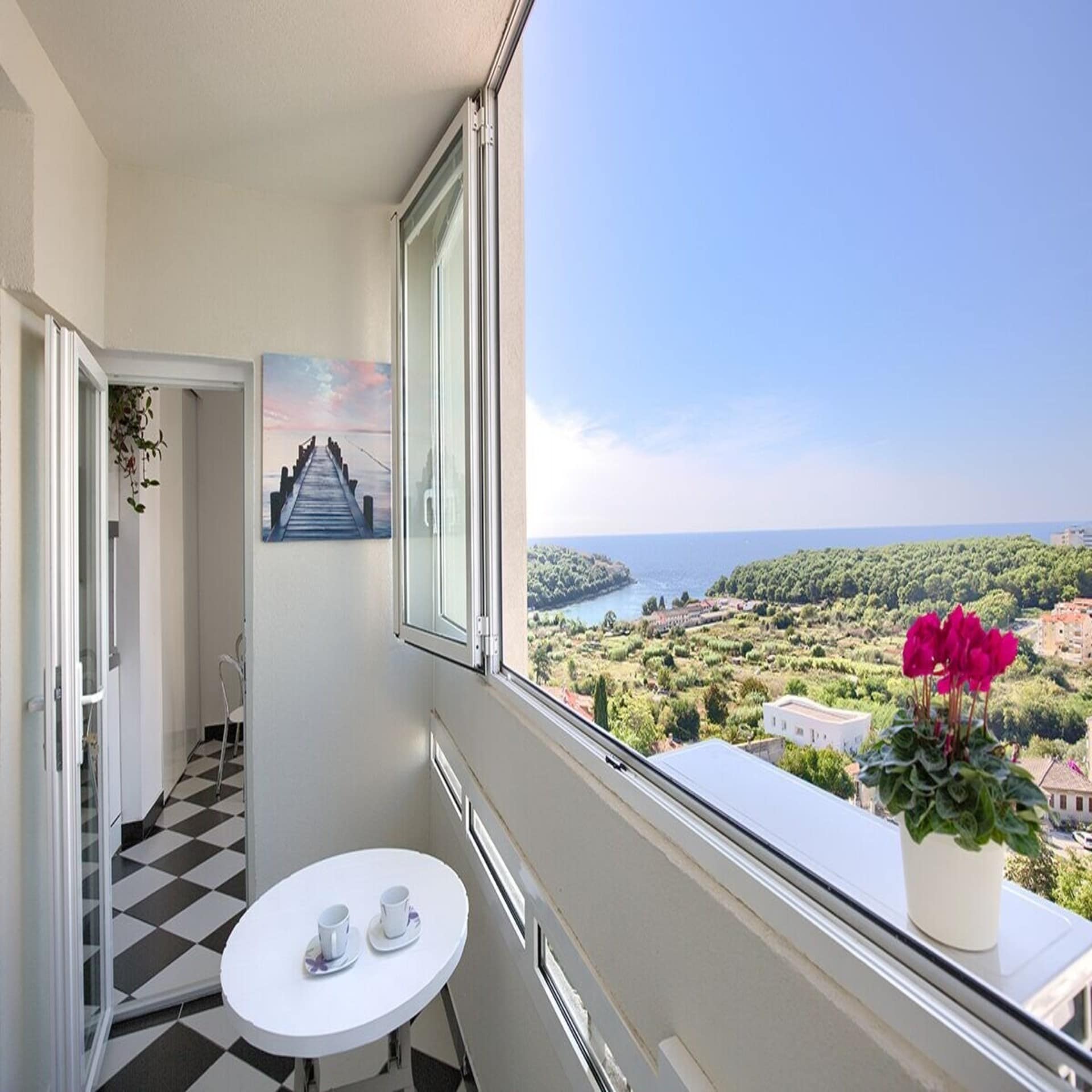 Seitlicher Blick: Eine Wohnung mit geöffnetem Fenster durch das man das Umland von Pula und das Meer sieht. 