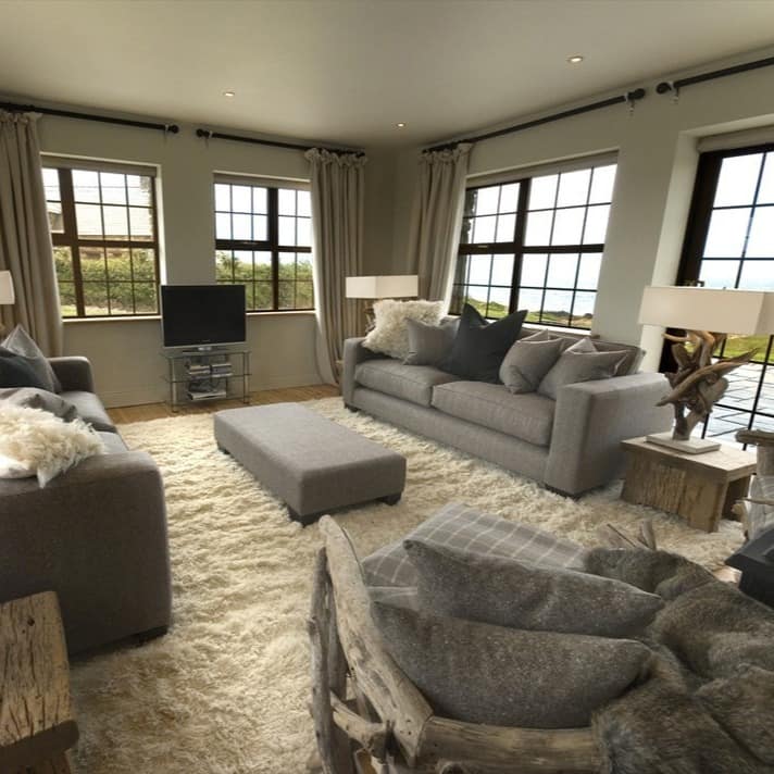 Das modern ausgestatte Wohnzimmer eines Luxus-Ferienhauses in Irland, durch die Fenster ist das Meer zu sehen