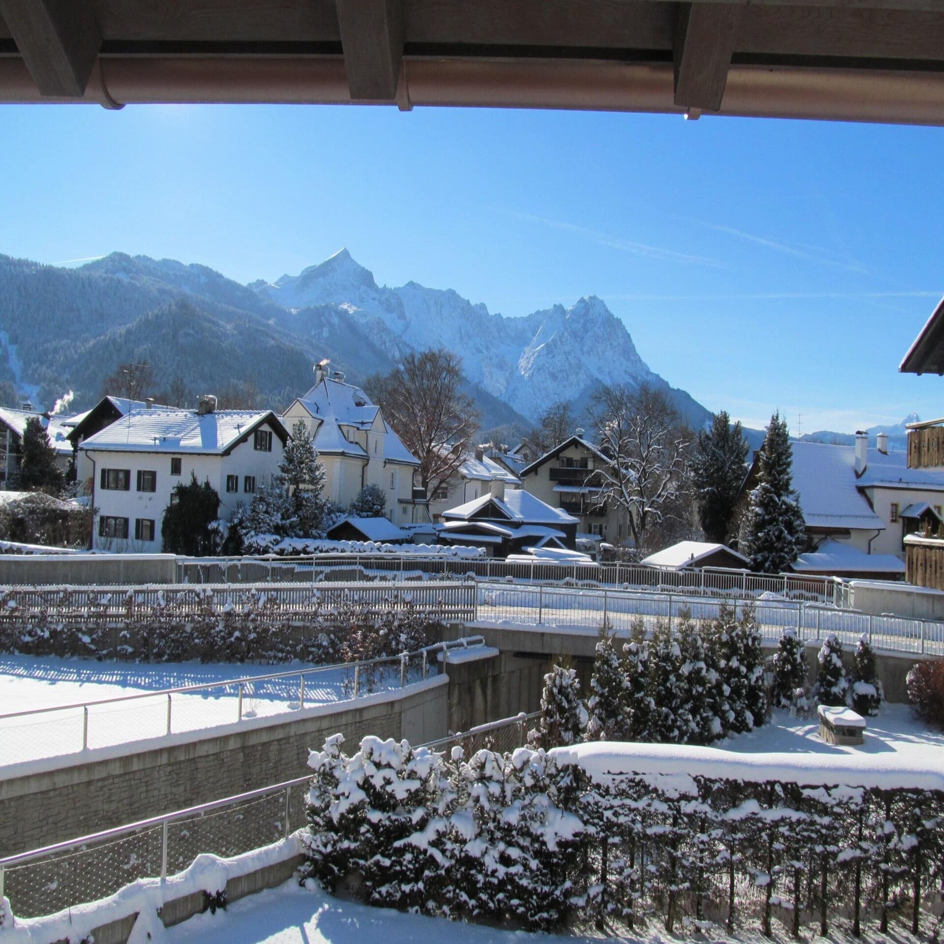 Blick von einem Balkon auf den Ort Garmisch-Partenkirchen. Die Sonne scheint, es liegt Schnee.