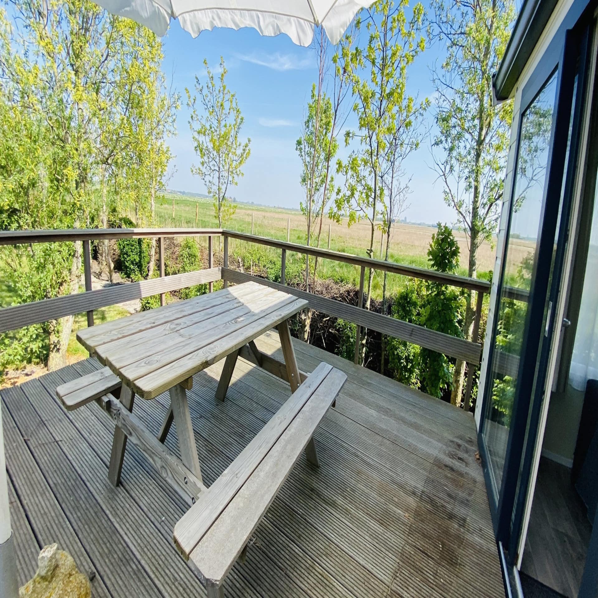 Holzveranda mit Sitzbank und Blick auf die sonnige, ländliche Umgebung. 