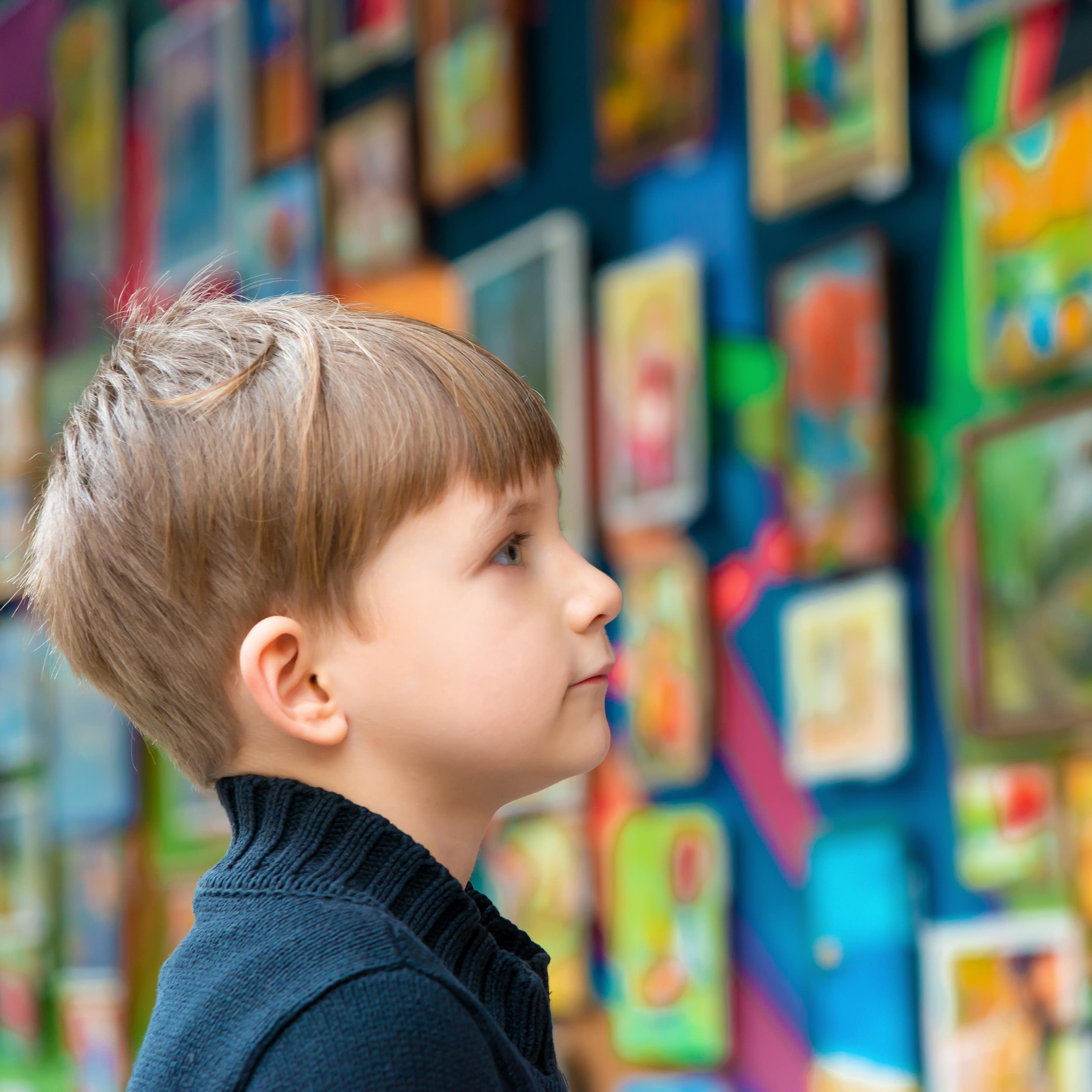 Ein blonder Junge betrachtet eine bunte Bilderwand.