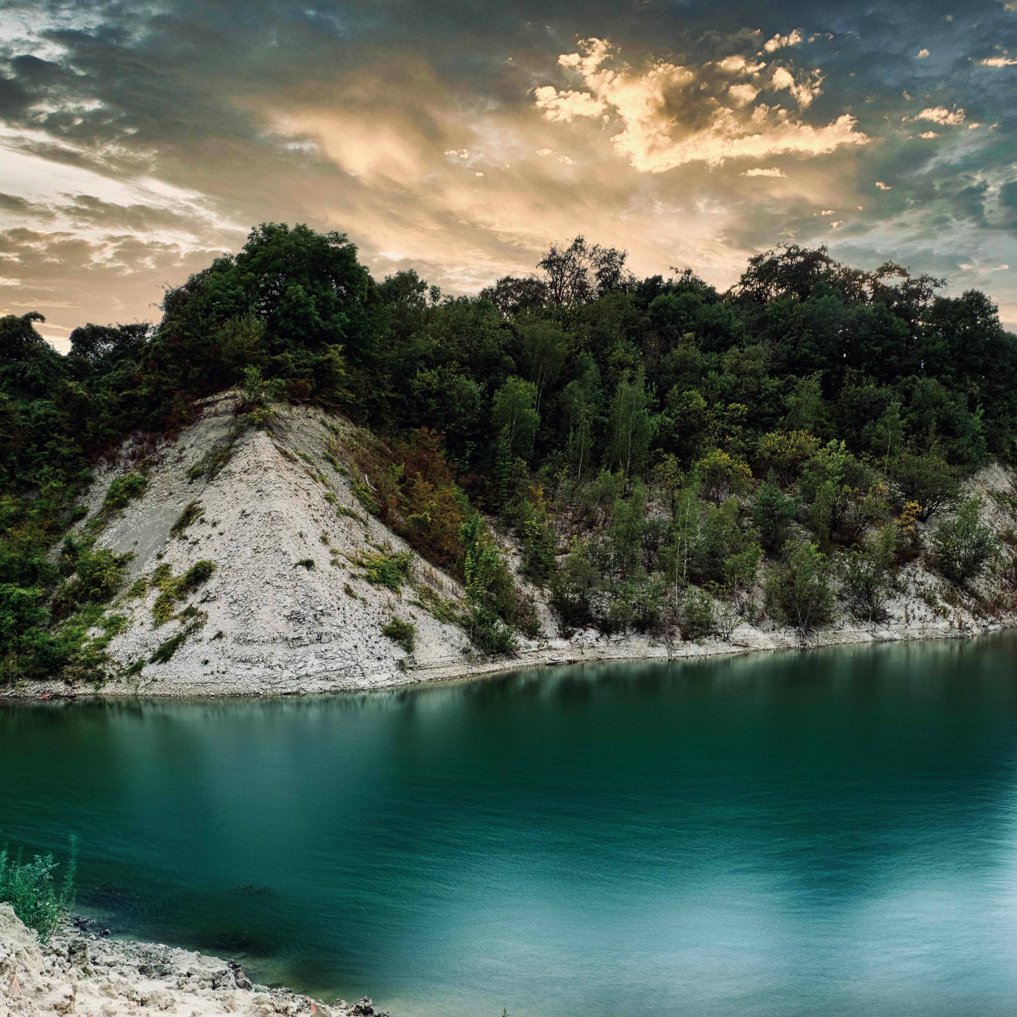 In der Abenddämmerung: Der türkisfarbene See in der Kiesgrube, umgeben von mit Bäumen bewachse-nen Kalkwänden.