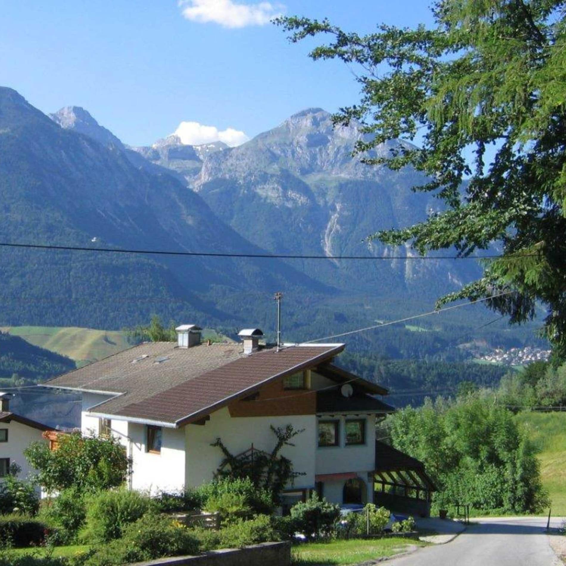 Dreistöckiges Haus vor hoch aufragenden Bergen in einer grünen Landschaft