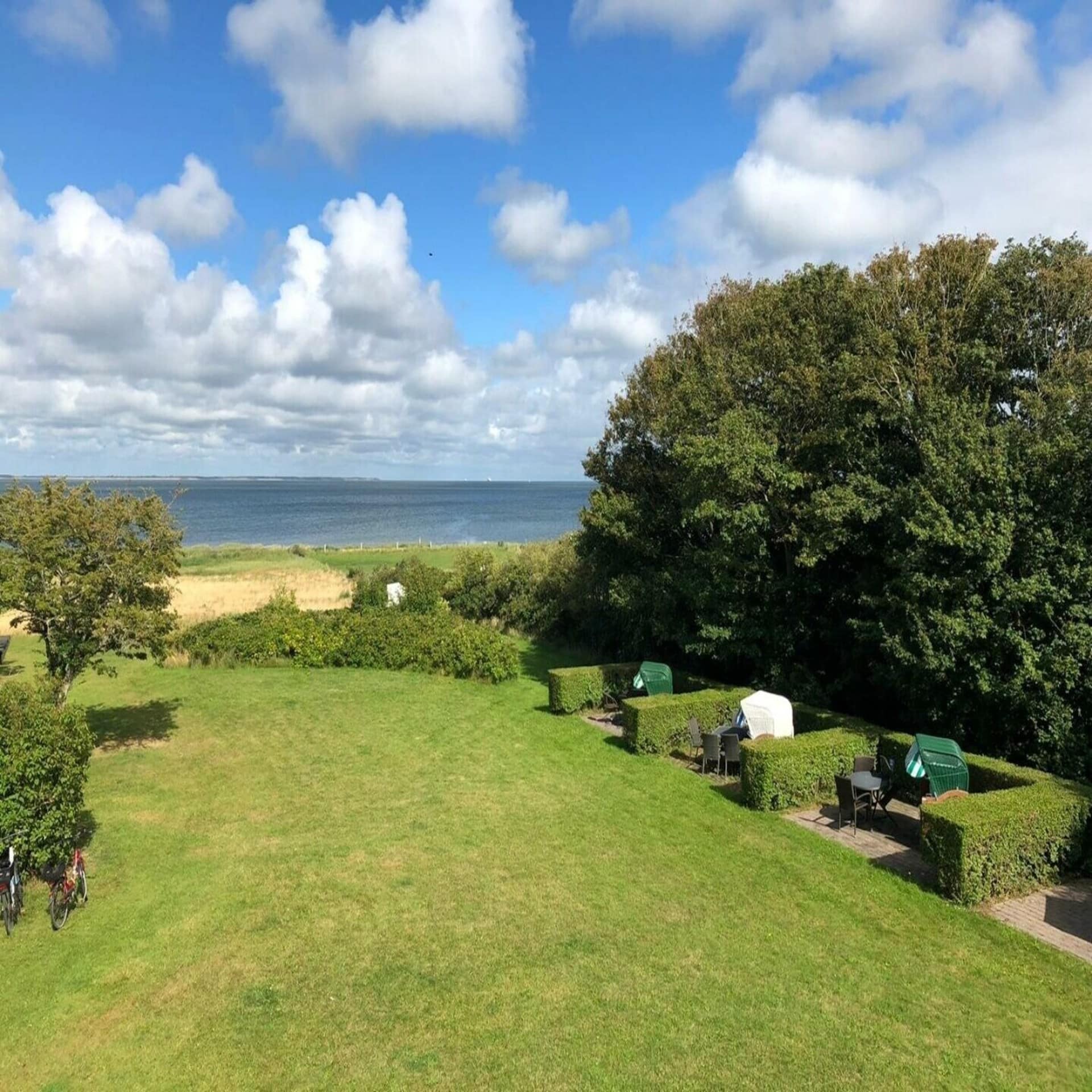 Großer, grüner Garten mit Sitzgelegenheiten und Zugang zum Strand.