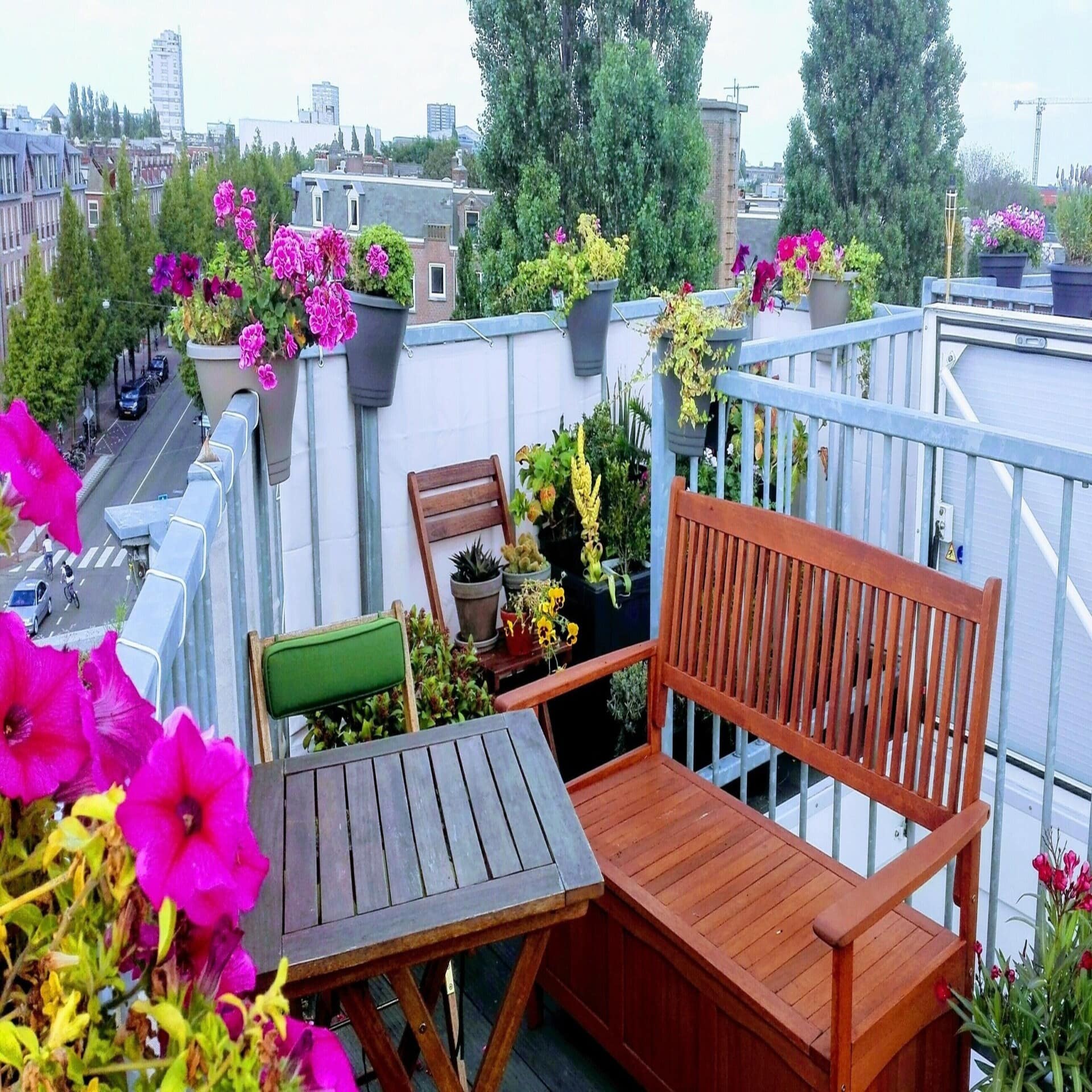 Dachterrasse mit Bank, Tisch und vielen Blumen sowie Blick über die Dächer von Amsterdam.