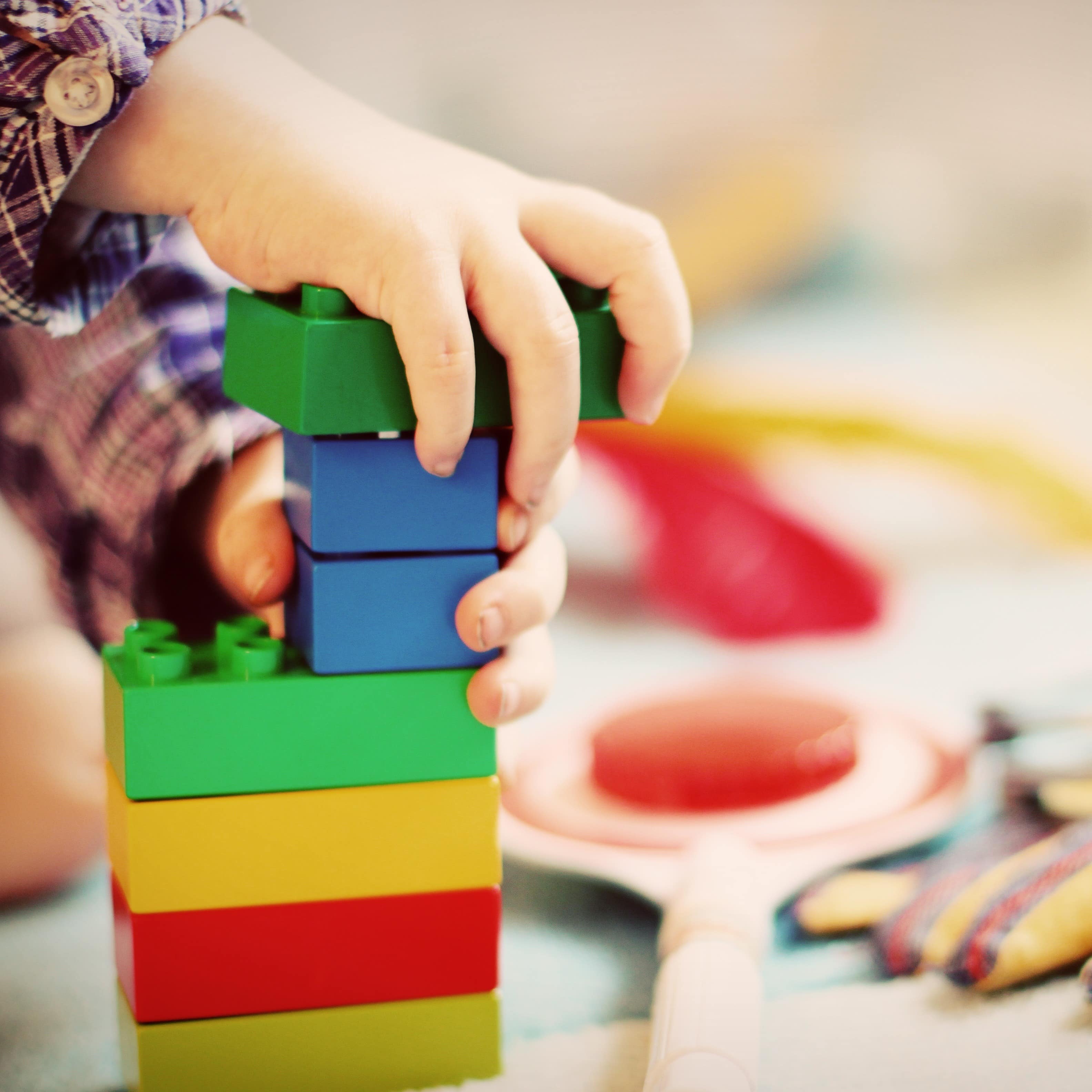 Nahaufnahme: Hände eines kleinen Jungen, der einen Duplo-Turm baut.