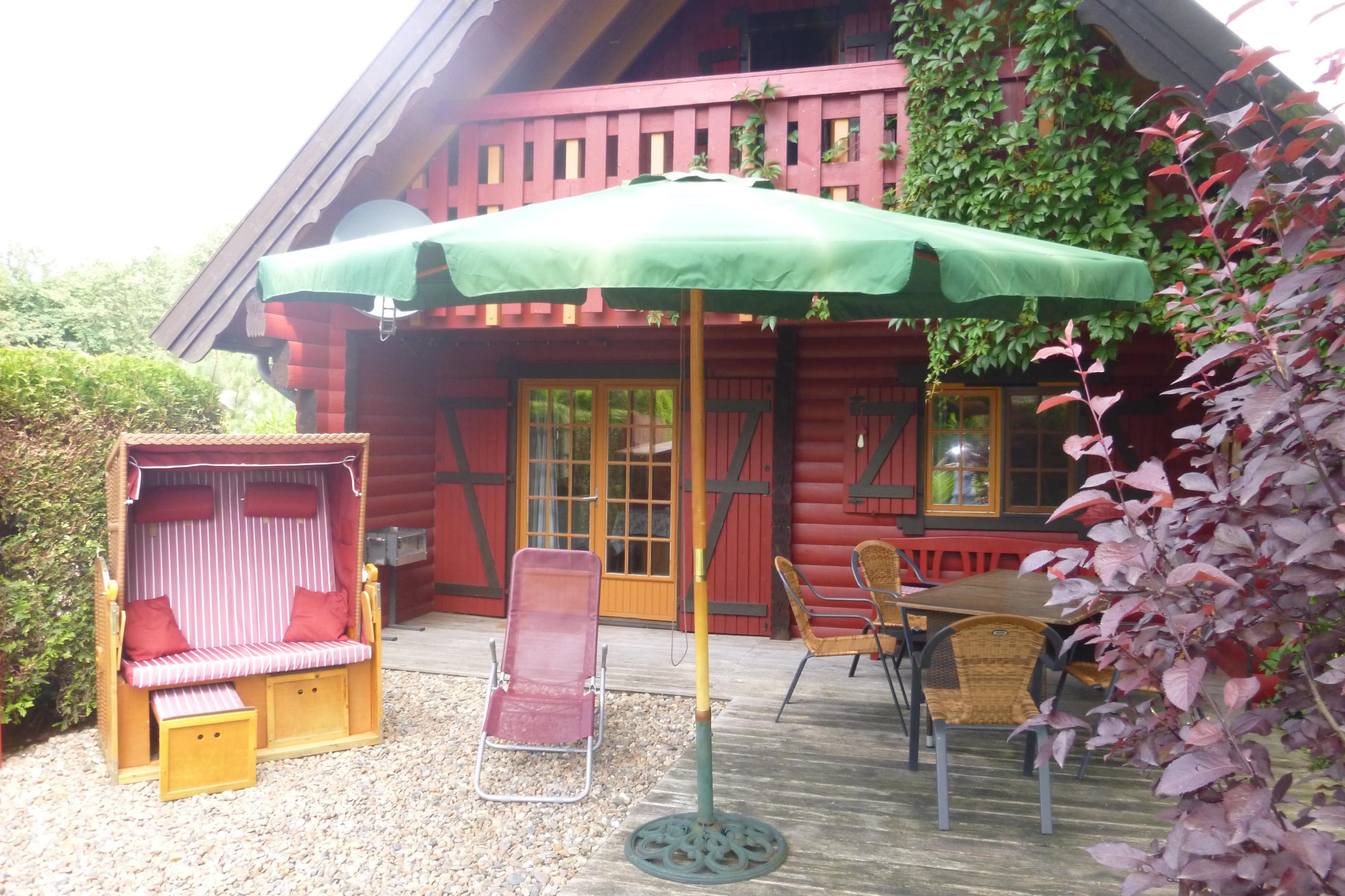 Rotes Holzhaus im Ferienpark mit Strandkorb, Sonnenliege und Sitzgelegenheiten