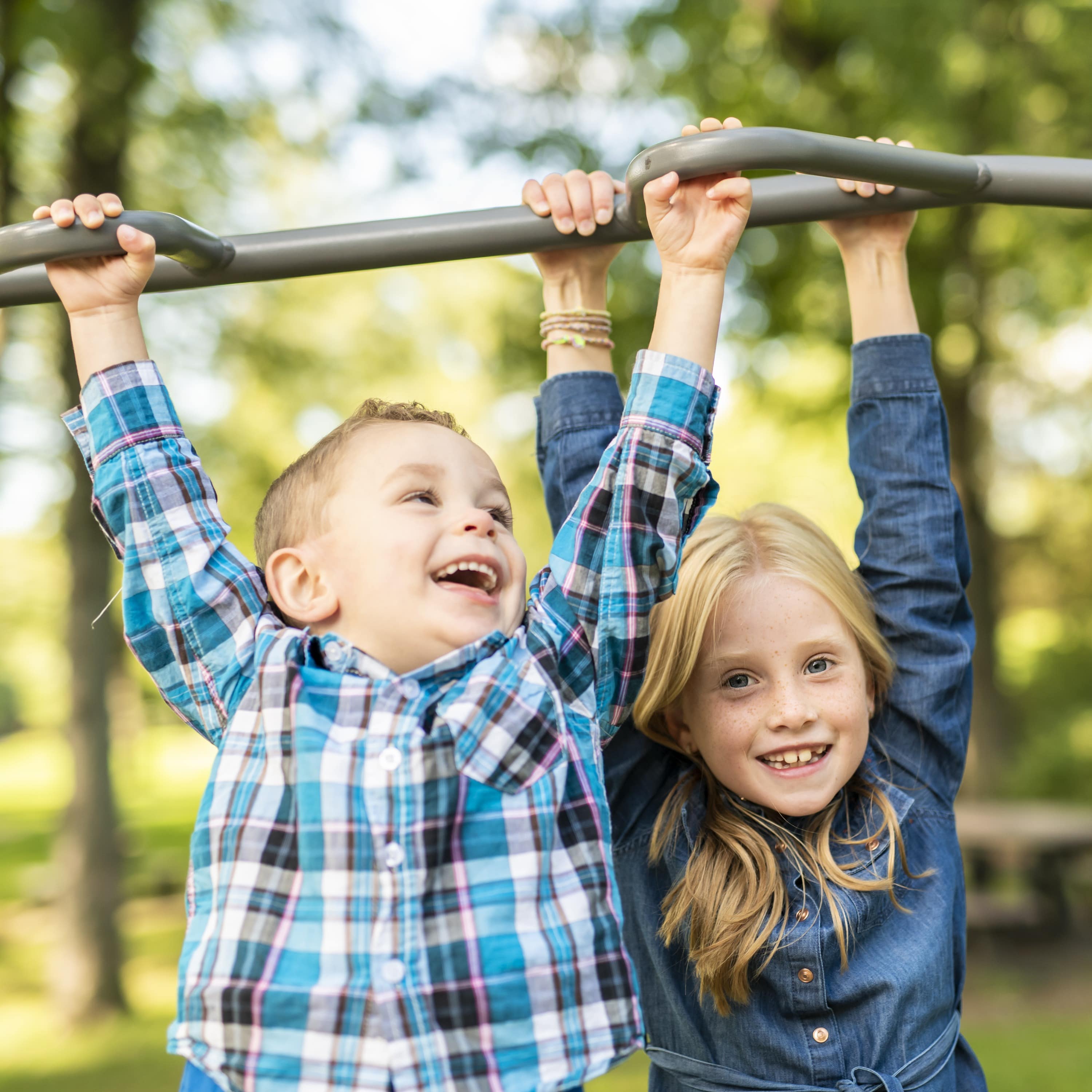 Ein Junge und ein Mädchen halten sich an einem Klettergerüst auf einem Spielplatz fest. Image URL: