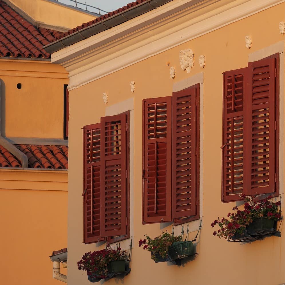 Nahaufnahme von Fensterläden eines Hauses, Blumenkästen hängen darunter.