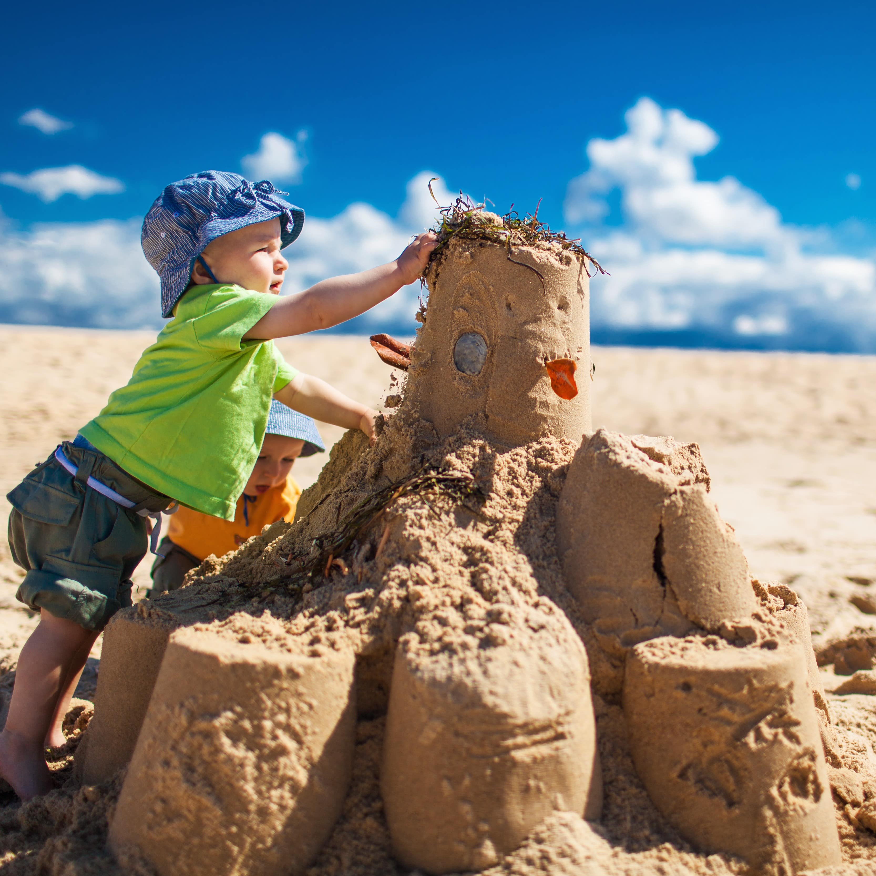 2 kleine Jungen bauen eine große Sandburg bei strahlendem Sonnenschein.