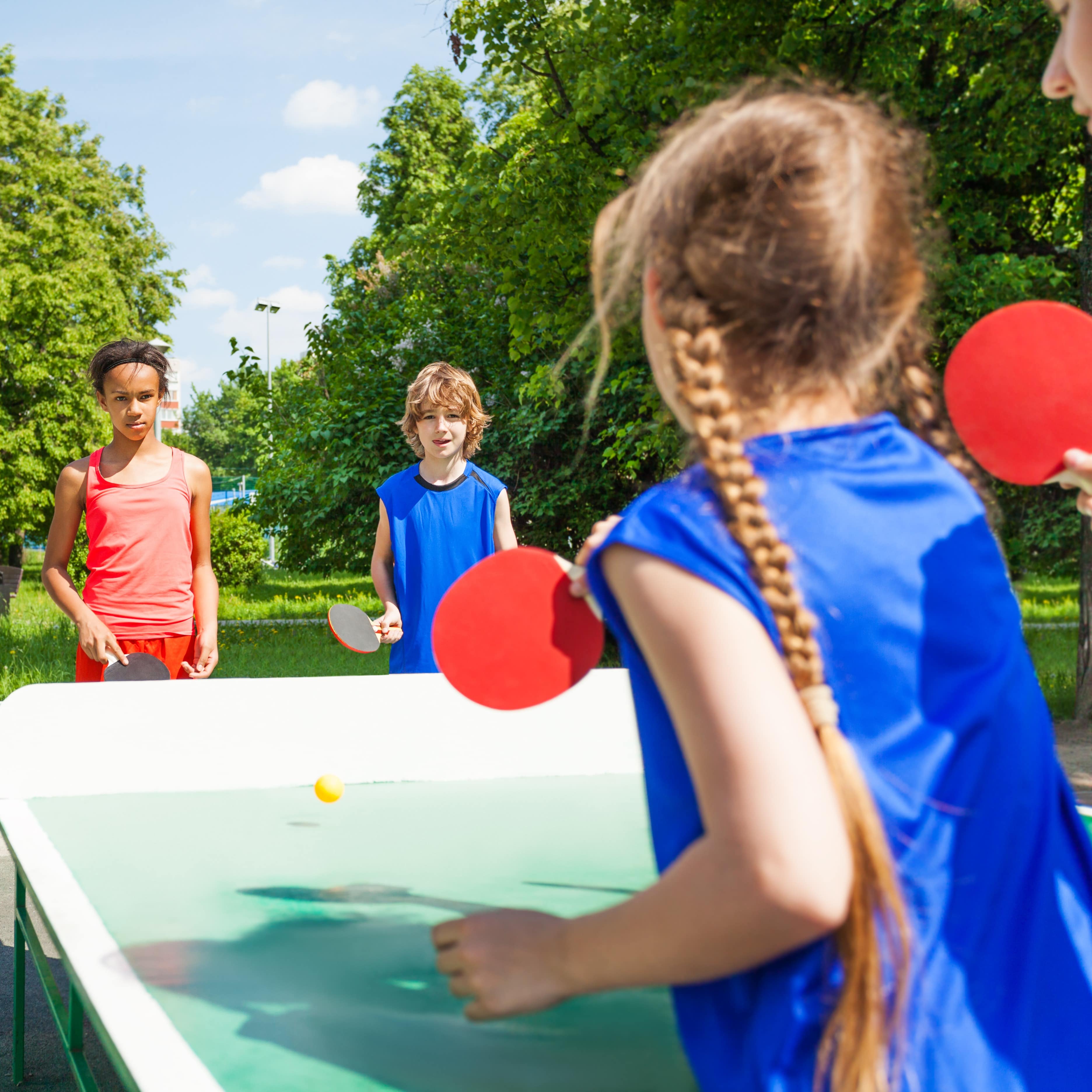 4 Kinder spielen draußen Tischtennis.