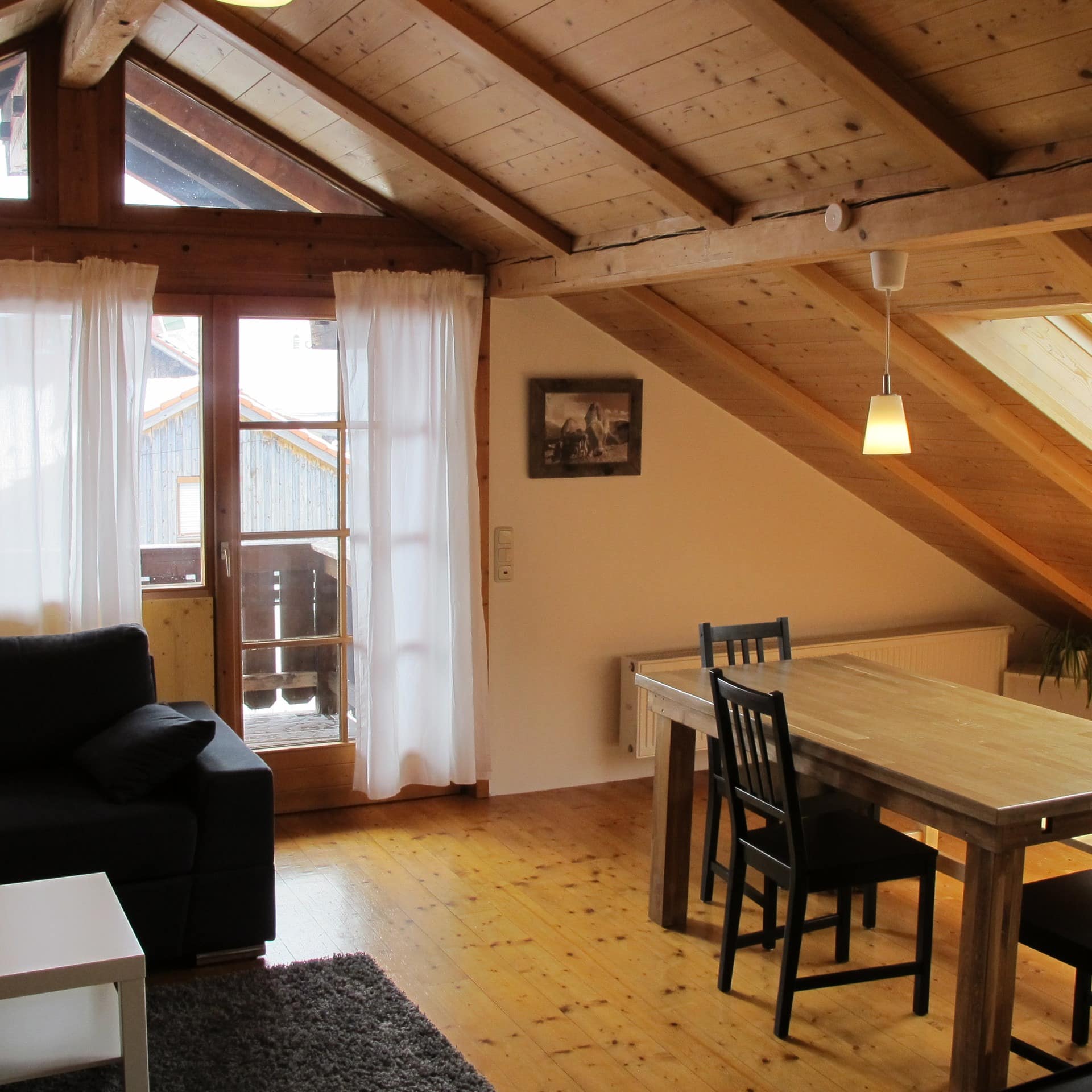 Wohnzimmer einer Dachgeschoss-Ferienwohnung mit Balkon in Pfronten, die Wände sind mit Holz verkleidet.