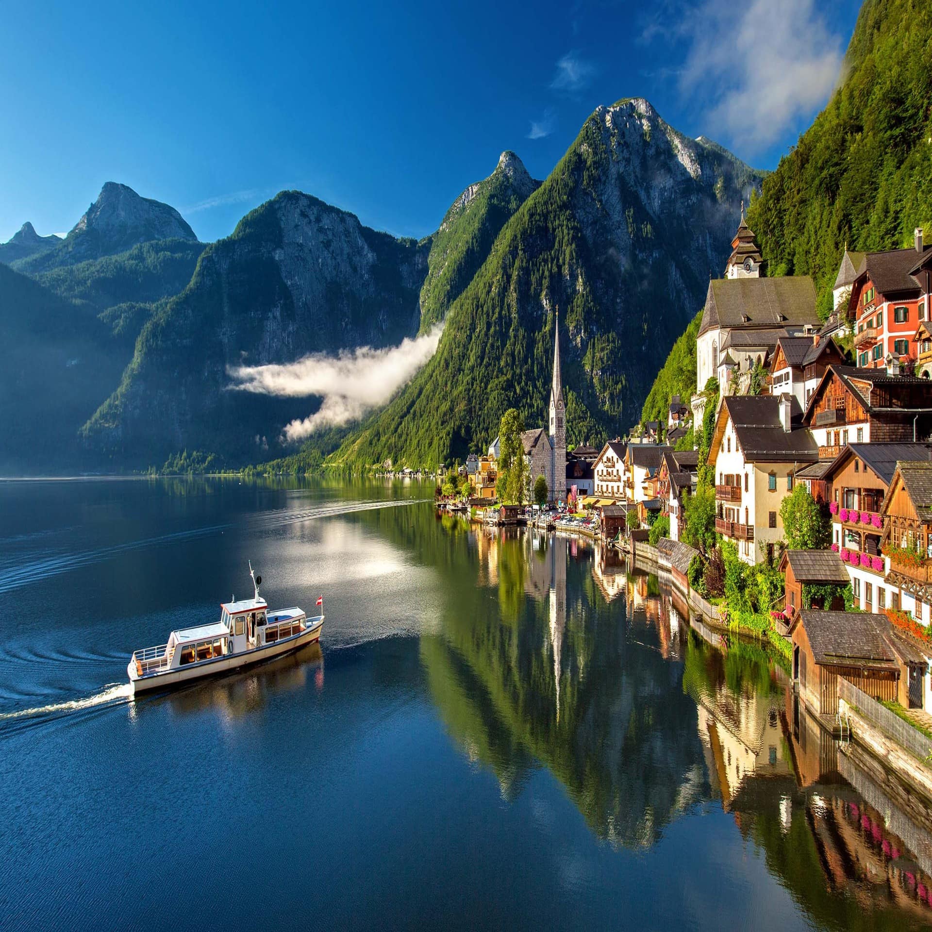 Blick über einen See mit Boot auf Hallstatt, das von Bergen umgeben ist.