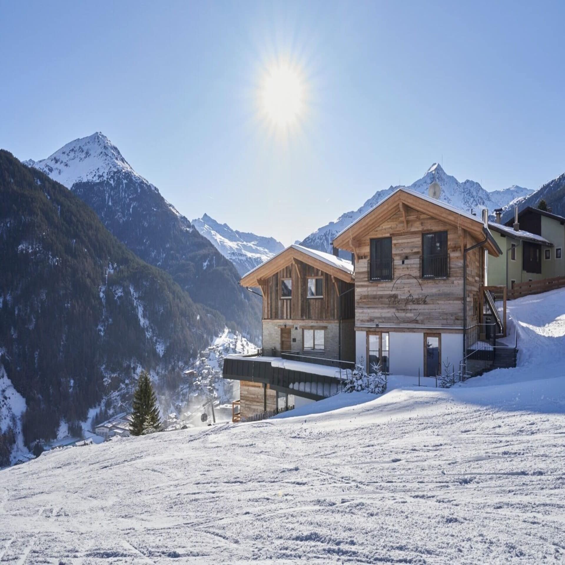 Urige Holzhütten an einer Skipiste in Tirol. Die Sonne scheint, es liegt Schnee.
