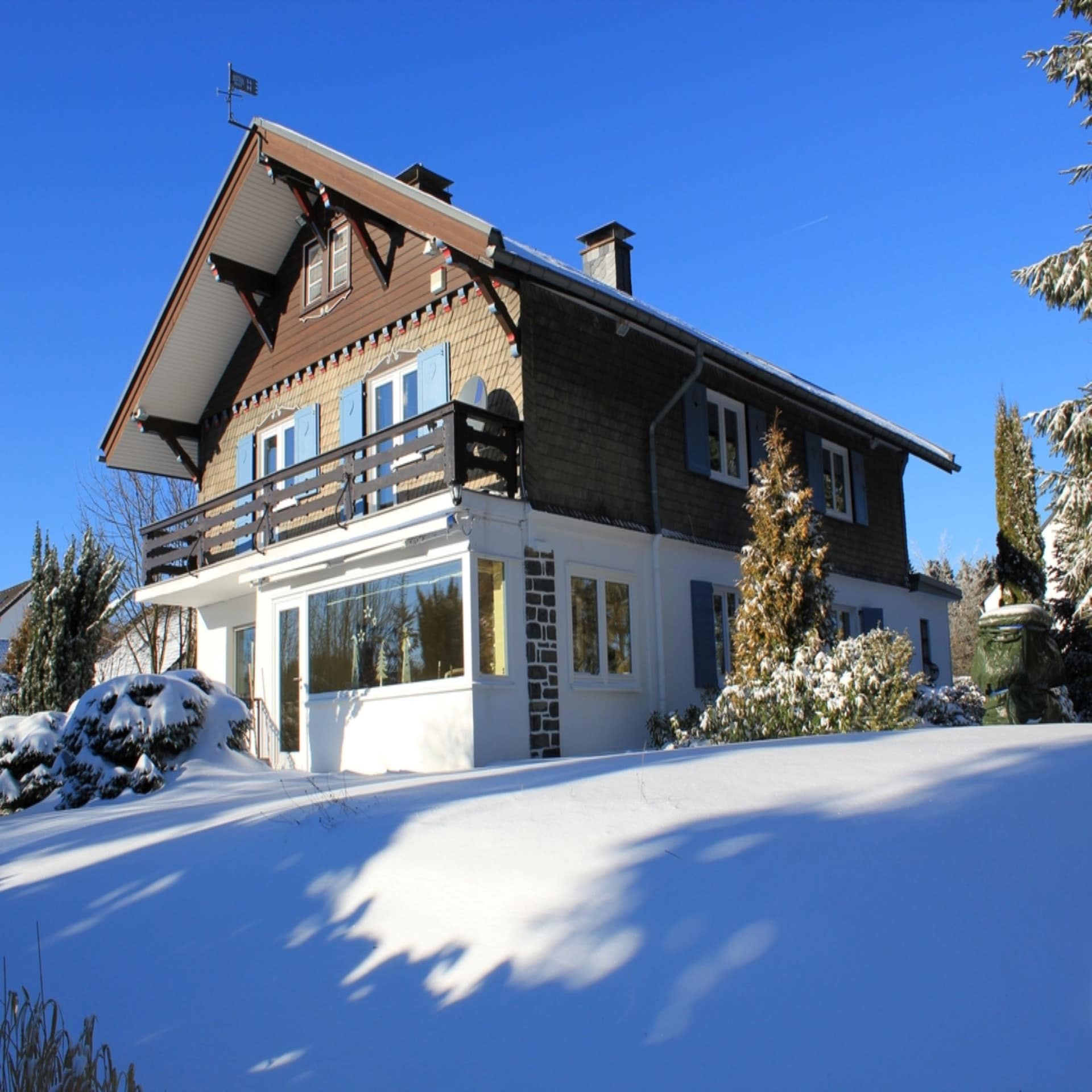 Landestypisches Haus in einem verschneiten Garten bei Sonnenschein.