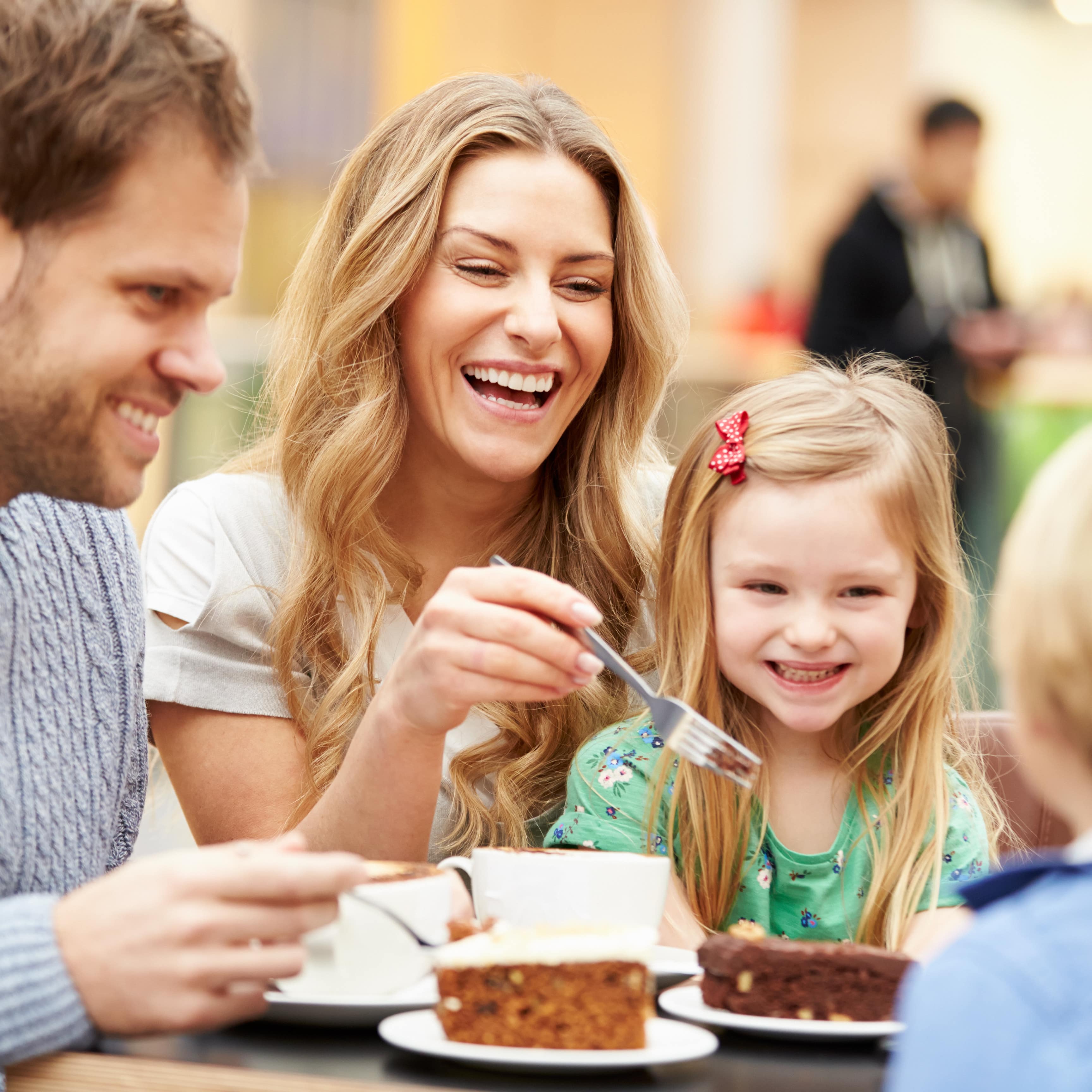 Im Café: Familie mit 2 Kindern sitzt bei Kaffeetrinken und isst Kuchen. 