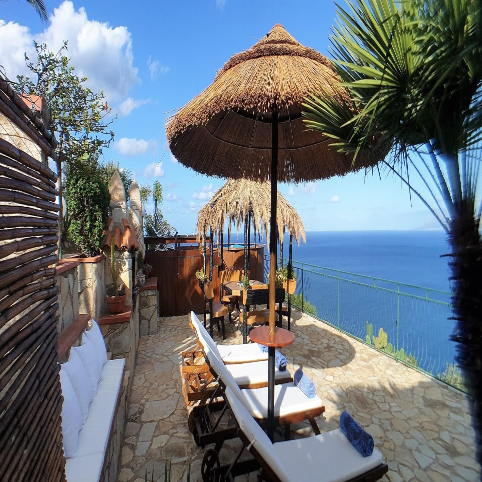 Großer Balkon mit Liegestühlen, Sonnenschirmen und Panoramablick auf das Meer.