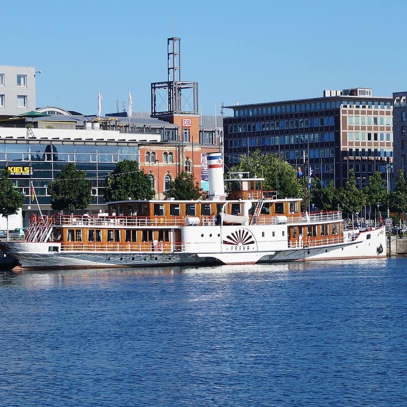 Blick vom Wasser auf die Innenstadt von Kiel, ein Ausflugsdampfer liegt vor Anker.