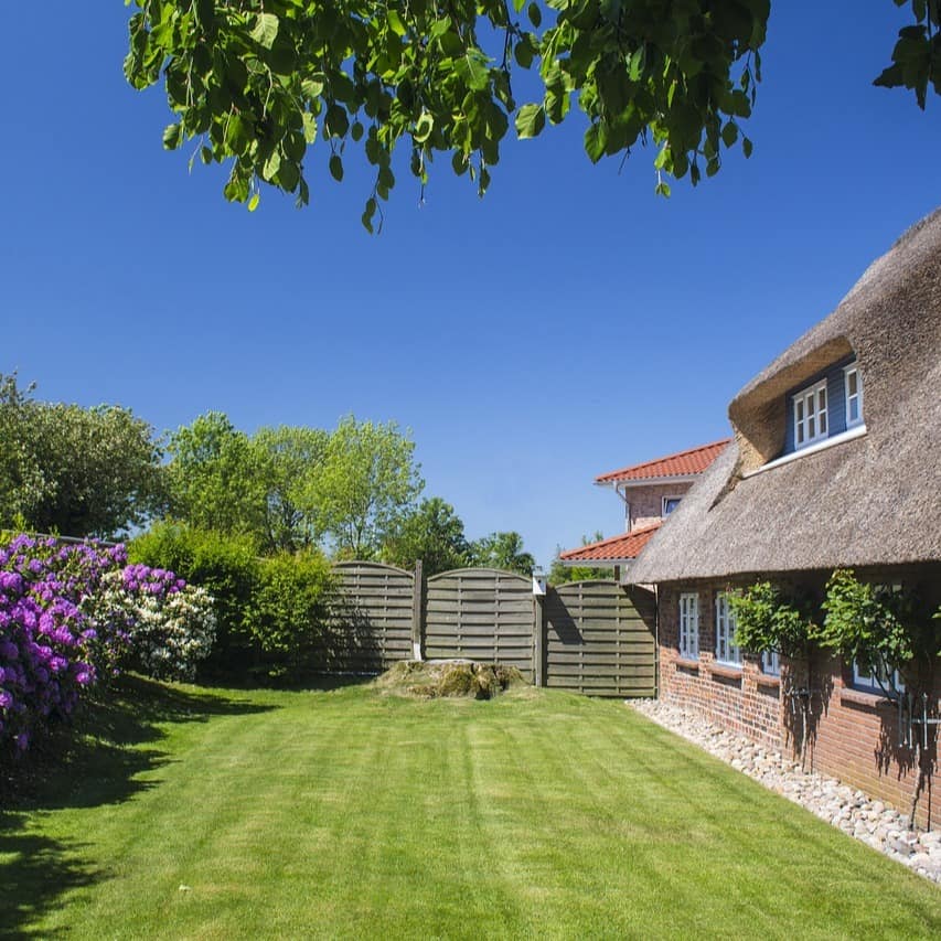 Ein Friesenhaus mit Reetdach und rotem Backstein sowie einem Garten.