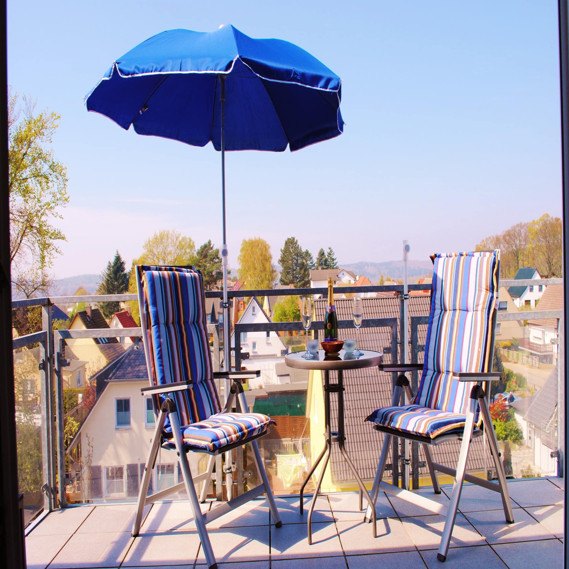 Dachterrasse mit 2 Stühlen, Sonnenschirm und Sekt sowie Blick auf den Ort Binz. 