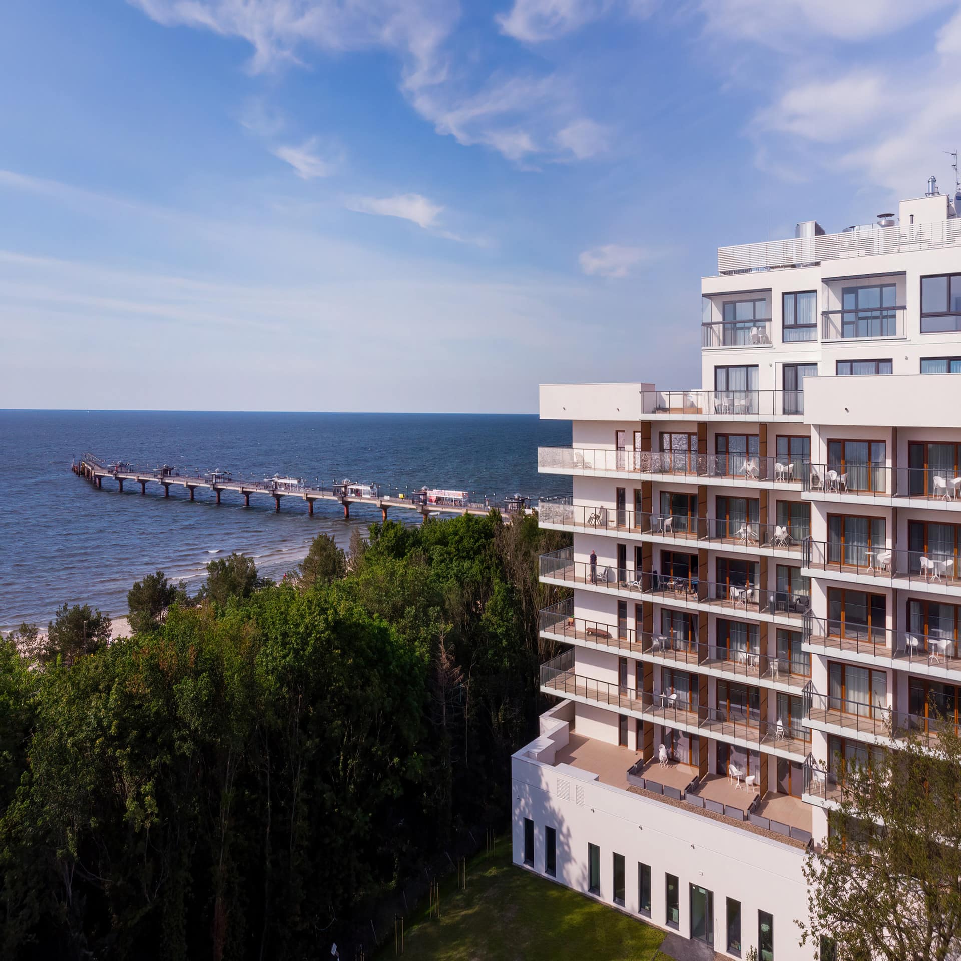 Apartmentblock direkt am Strand, Bäume sind zwischen dem Haus und dem Strand. Blick auf die Seebrücke. 