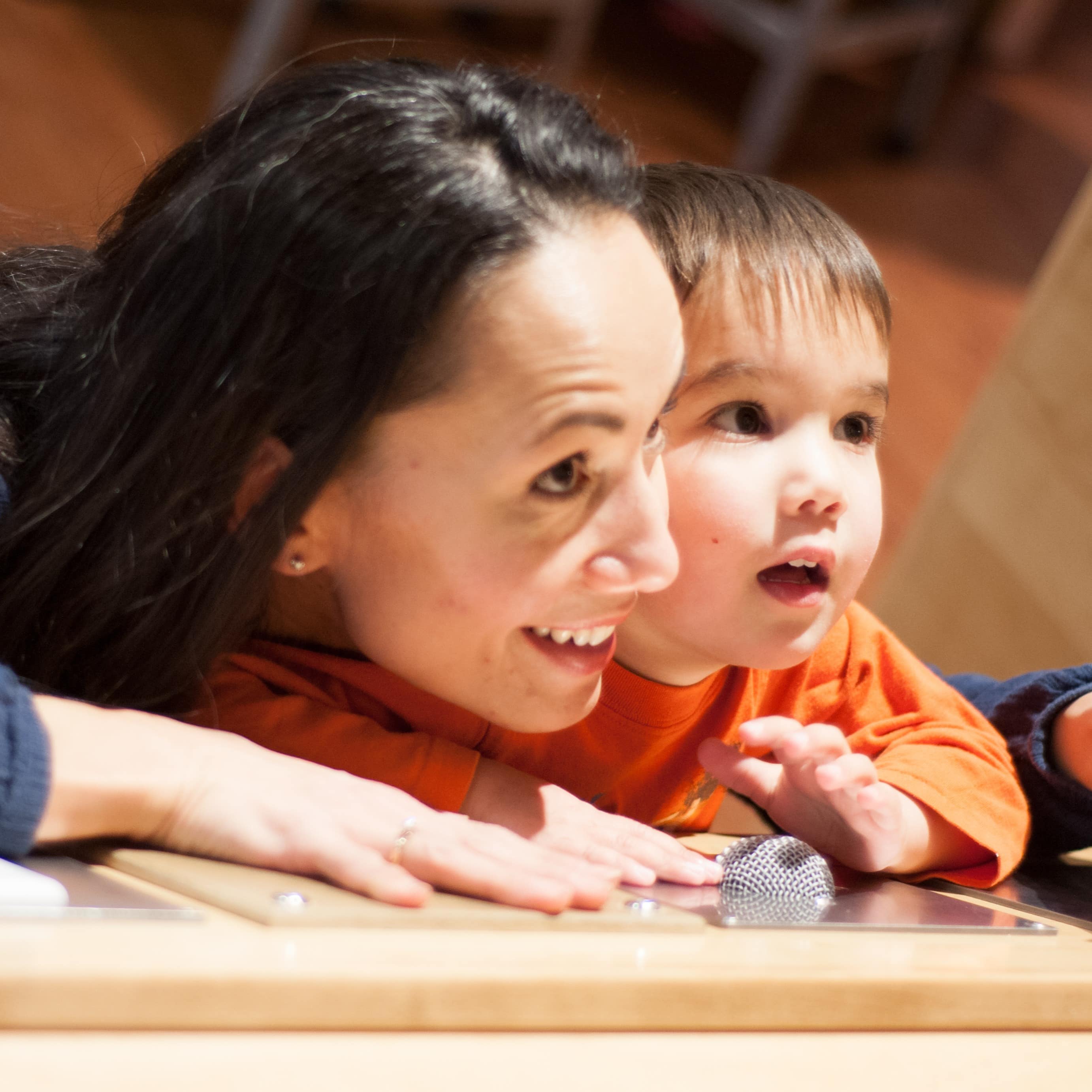 Mutter und kleiner Sohn beobachten etwas außerhalb des Bildes, sie stehen vor einer Platte mit Knöpfen.