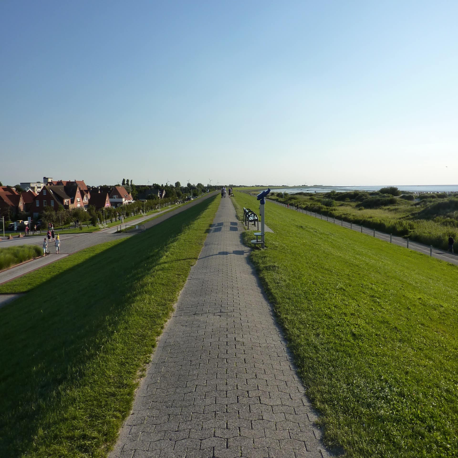 Blick entlang des Deichs in Norden-Norddeich. Rechts das Meer, links Häuser und eine Straße.