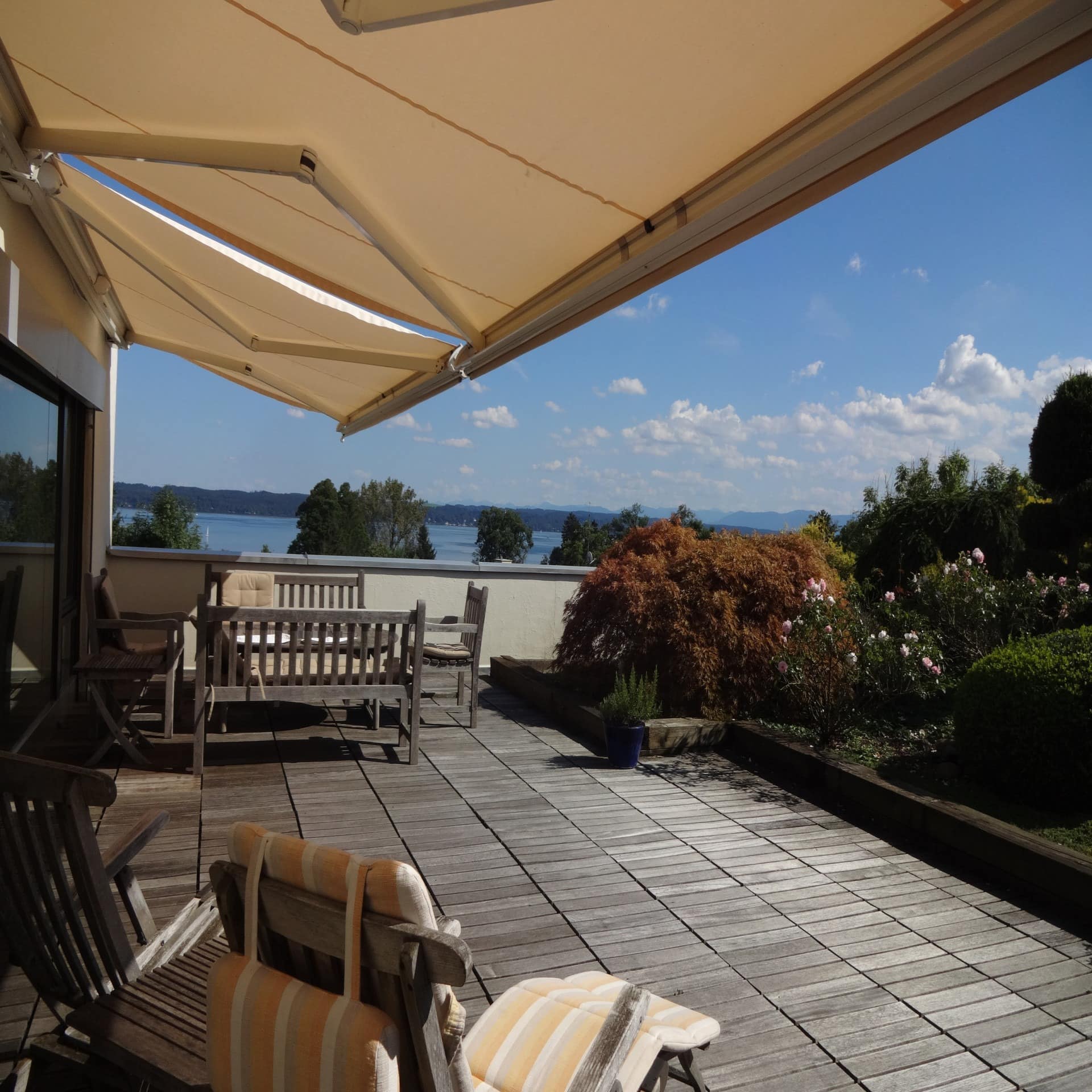 Terrasse mit Liegestühlen, Markise und Garten sowie Blick auf den Starnberger See.