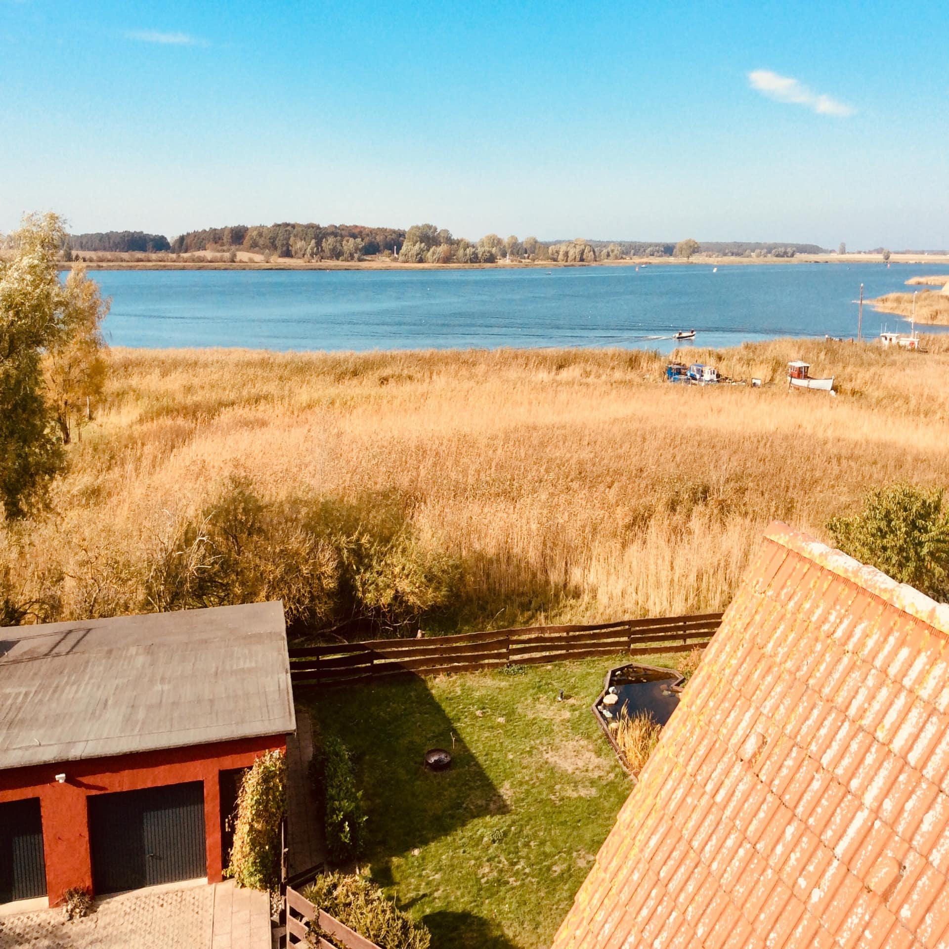 Blick aus dem oberen Stockwerk eines Hauses auf den Garten, einen Schilfgürtel und das Wasser der Peene. 