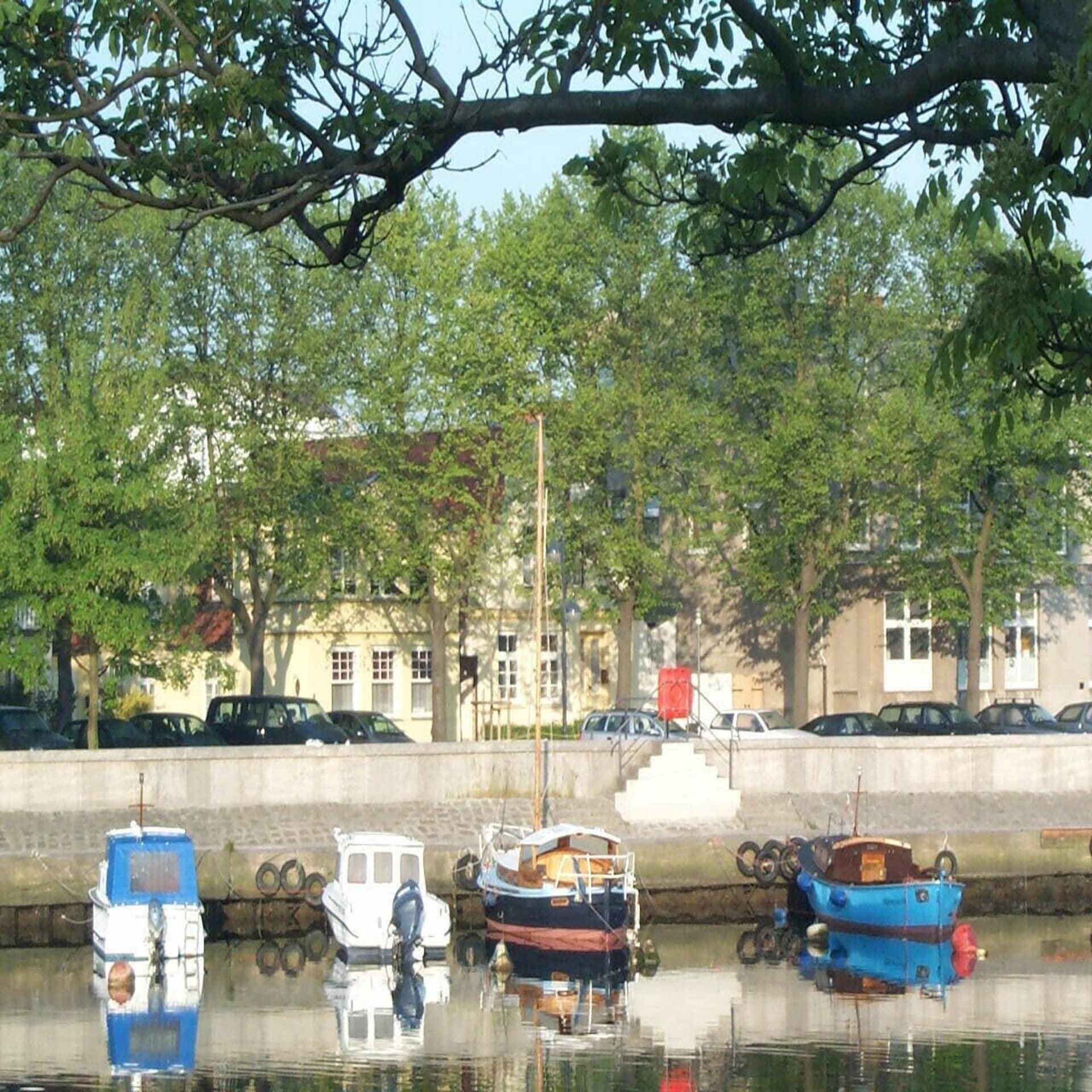 Blick über den Strom, kleine Boote liegen vor Anker, dahinter Bäume und Häuser.