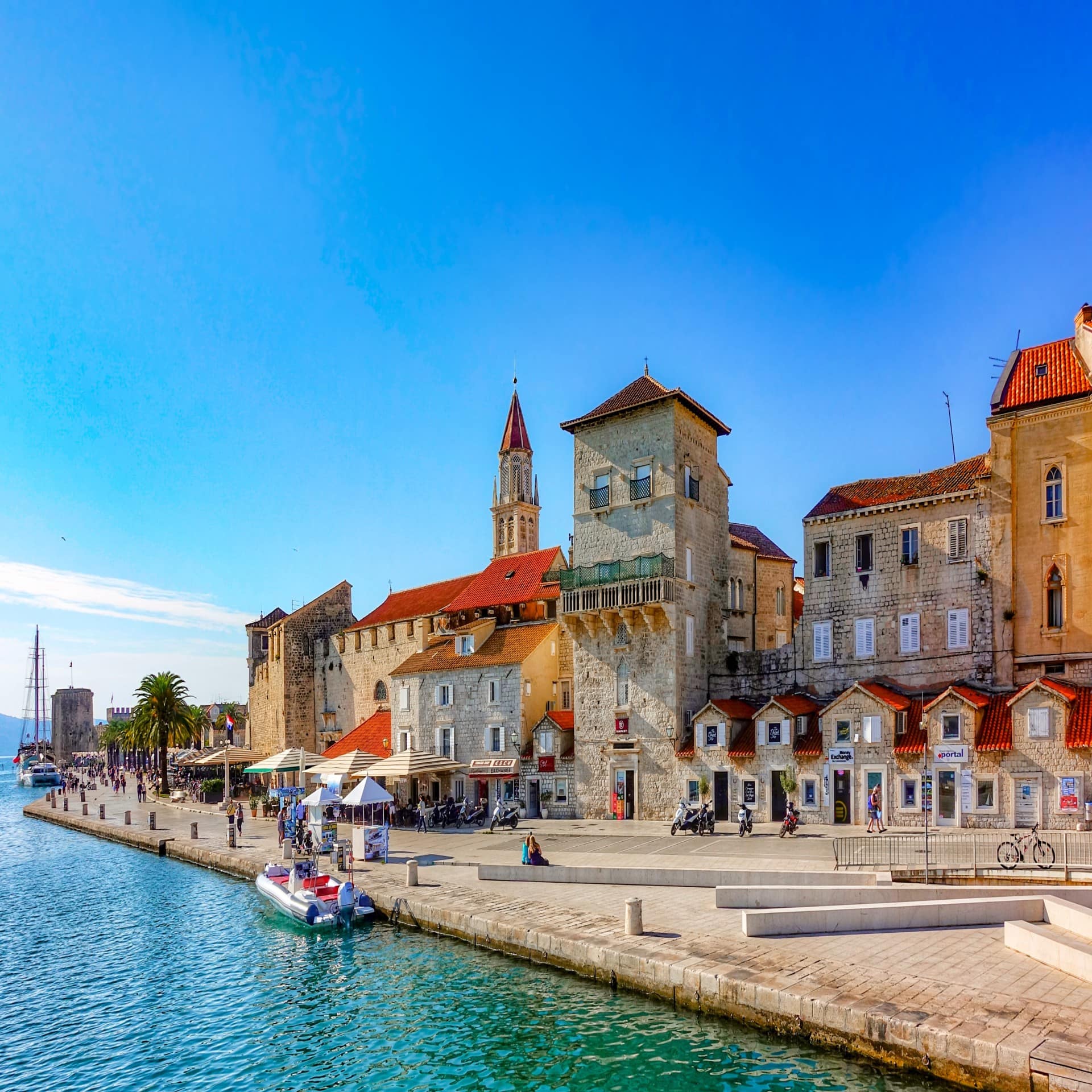 Blick vom Wasser auf die Altstadt und den Bootsanleger von Trogir bei Sonnenschein. 