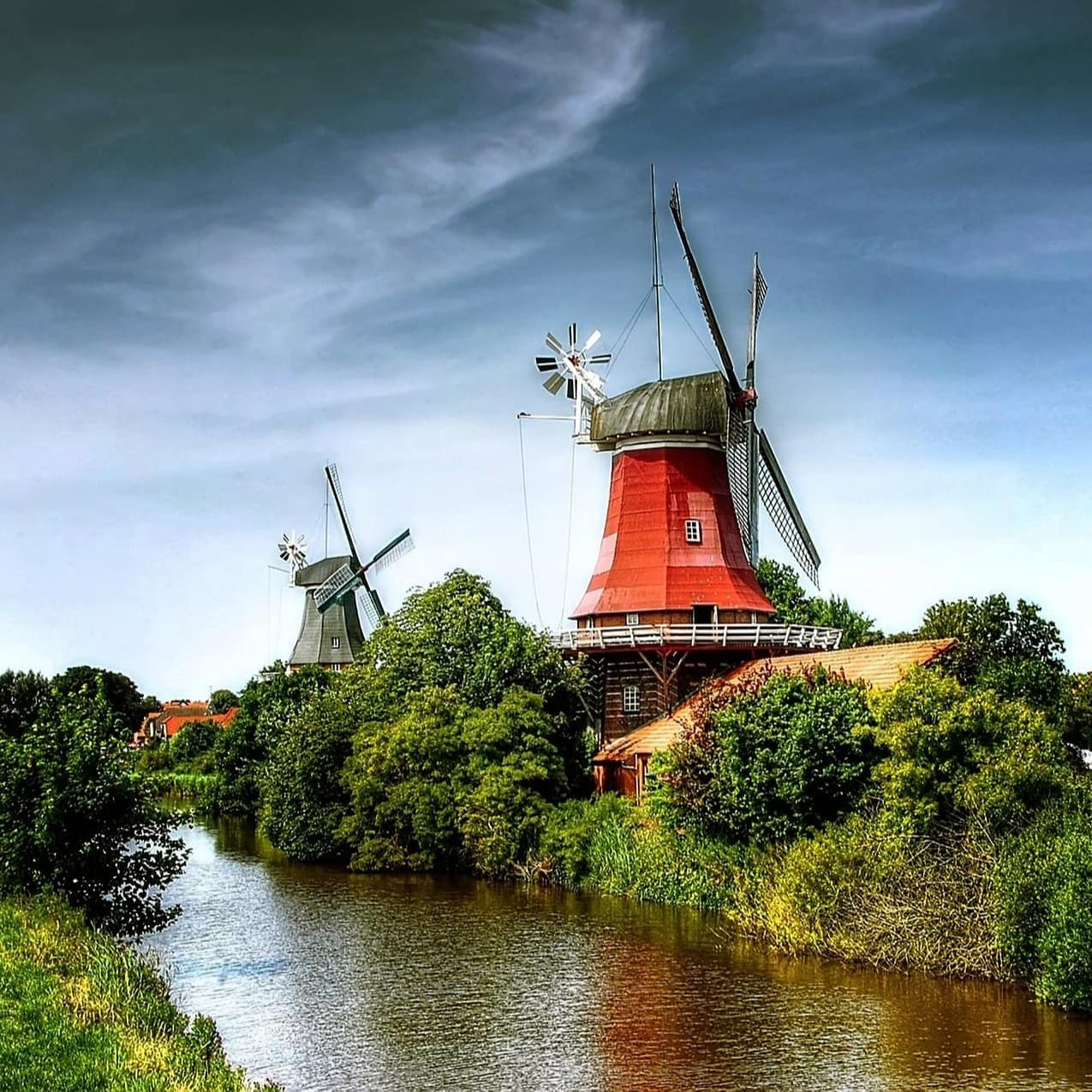 Ostfriesische Landschaft mit Häusern und Windmühlen am Wasser inmitten von Bäumen