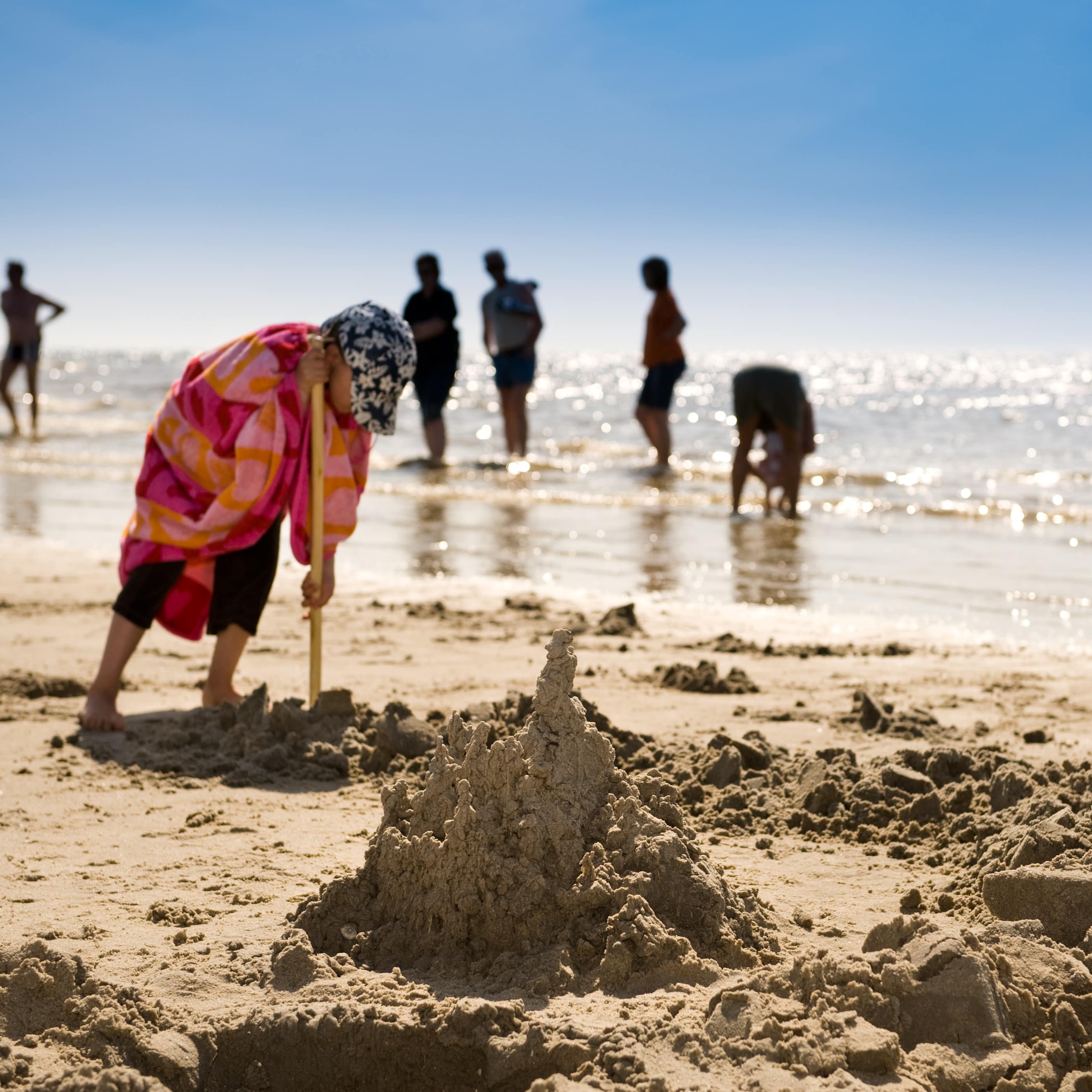 Ein kleiner Junge mit Mütze und Handtuch baut eine Sandburg am Strand.