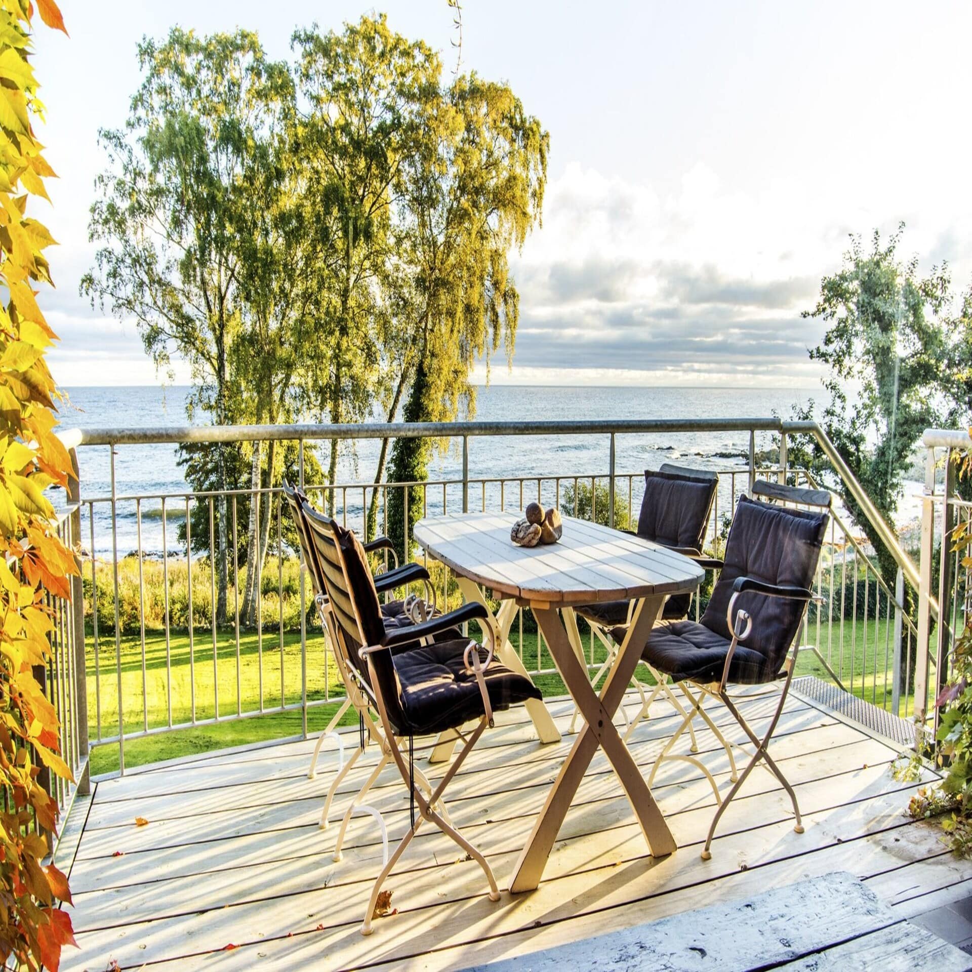 Terrasse mit Tisch und 4 Stühlen in einem Garten direkt am Meer mit Blick auf das Meer. 