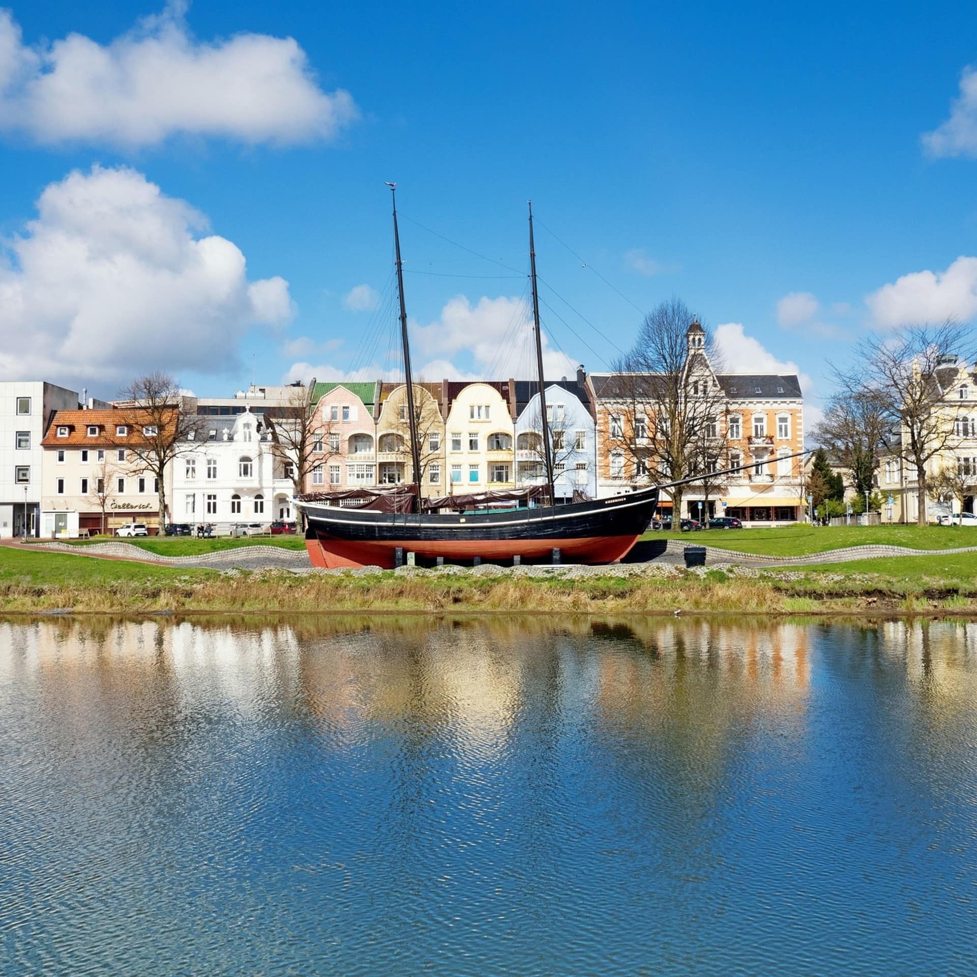 Blick vom Wasser auf ein Segelschiff am Ufer mit schönen Häusern dahinter