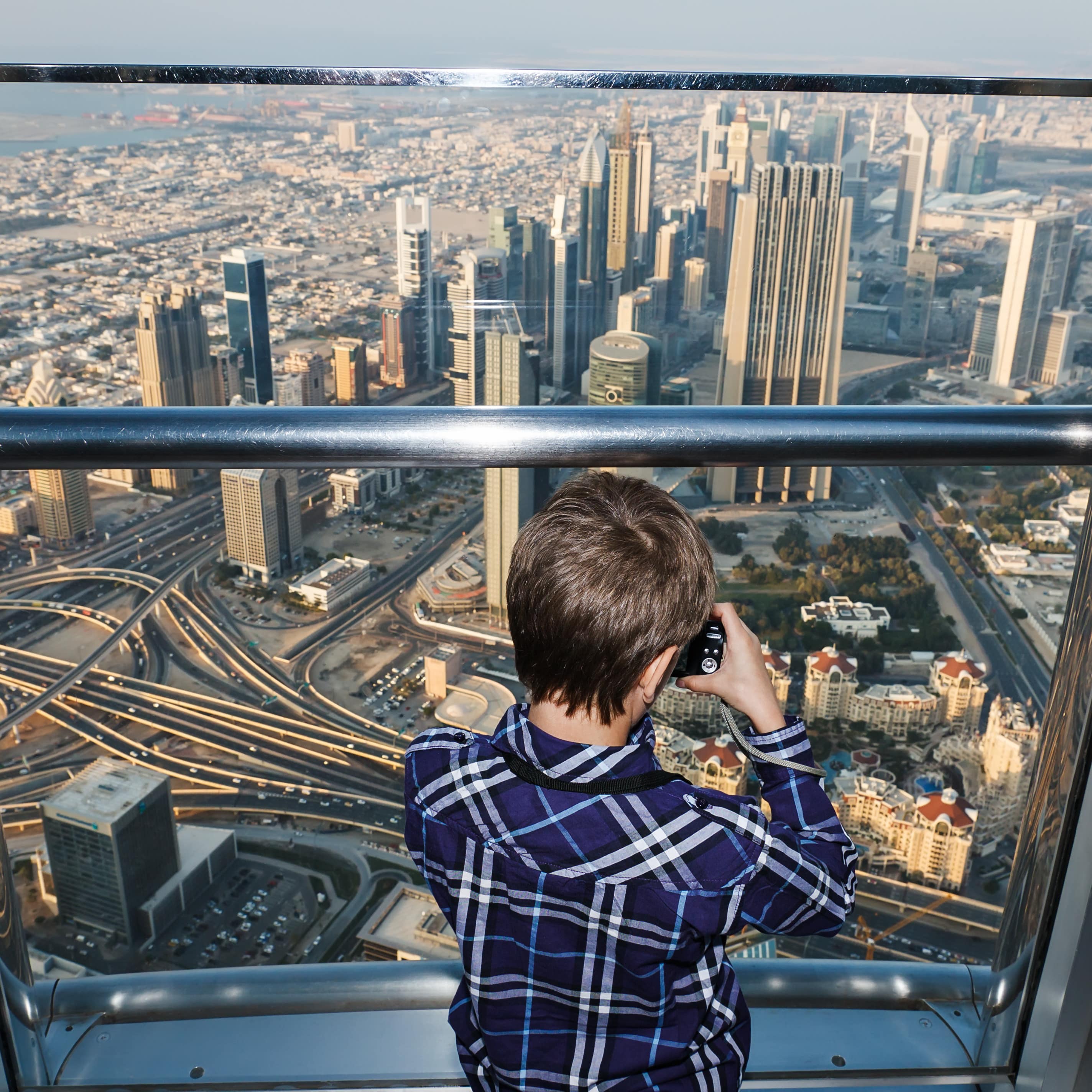 Rückenansicht: Ein Junge auf der Aussichtsplattform des Burj Khalifa macht ein Foto.