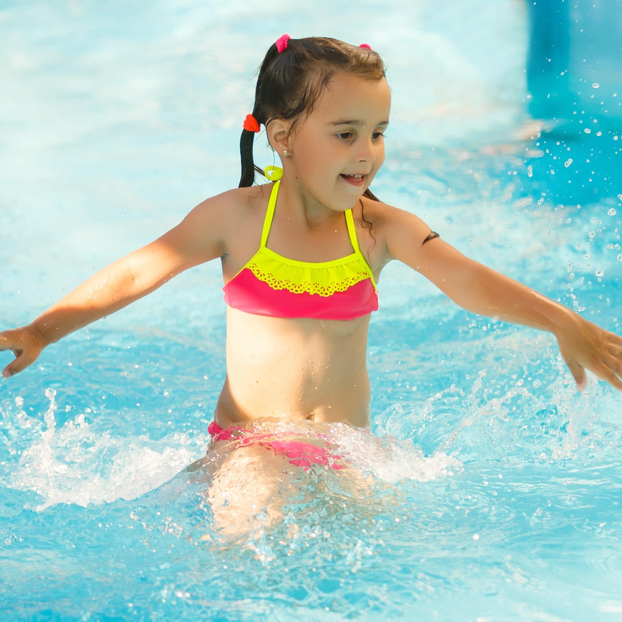 Mädchen in einem gelb-pinken Bikini im Wasser eines Schwimmbads.
